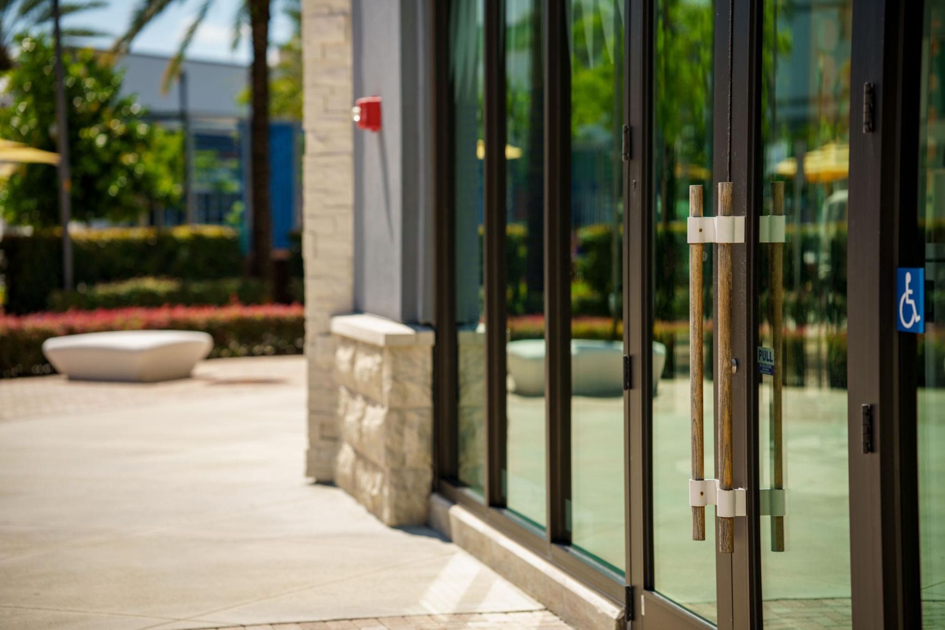 Glass doors with metal handles next to a stone wall and a concrete walkway. A blue handicap symbol is on the door.