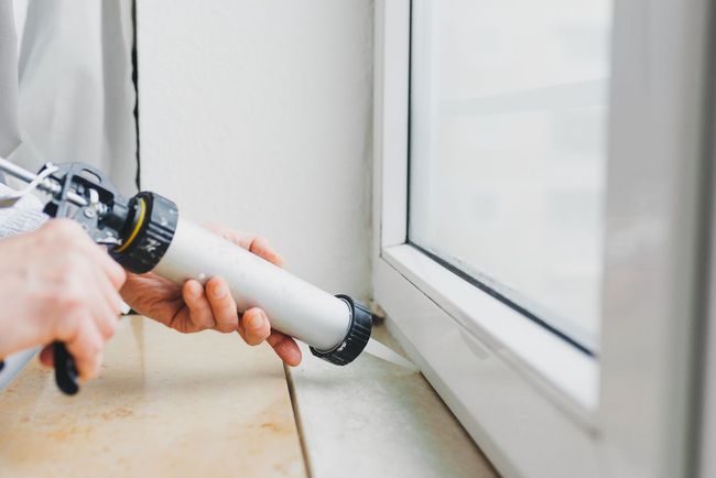 Application de mastic blanc le long du bord d'un cadre de fenêtre à l'aide d'un pistolet à calfeutrer