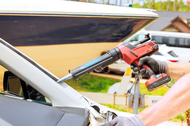 Un ouvrier utilise une perceuse sans fil rouge pour retirer le joint d'étanchéité d'un pare-brise de voiture à l'extérieur.