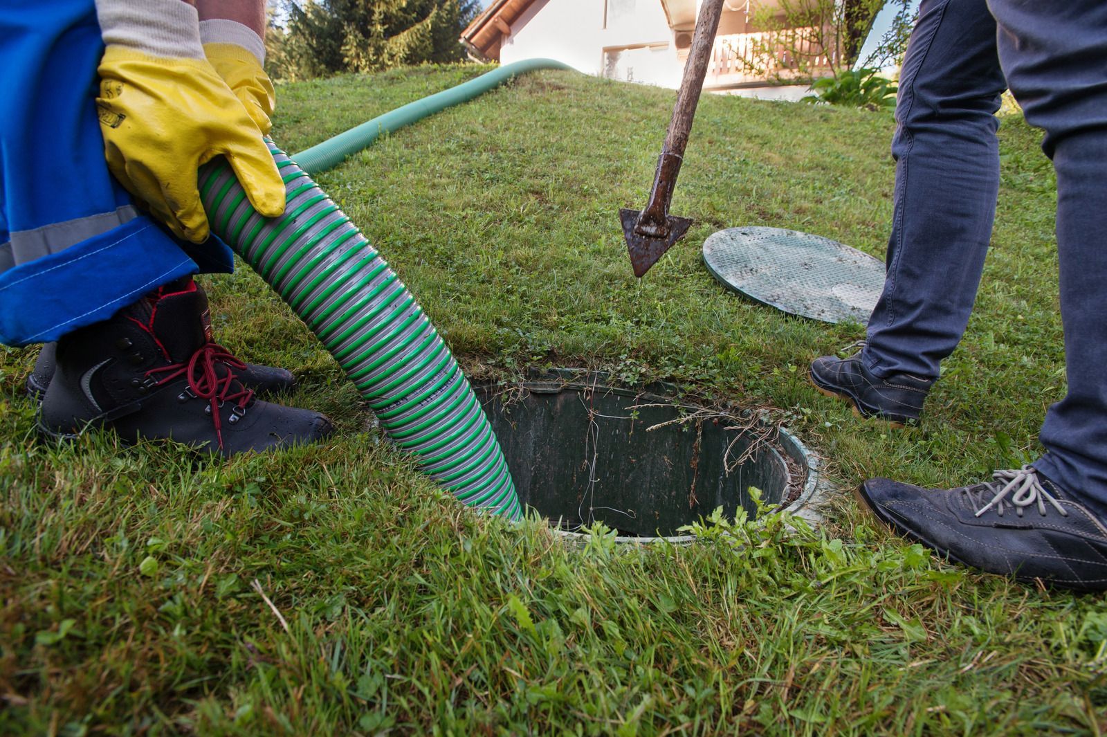 Workers using a hose and shovel to clean a grassy yard drain hole
