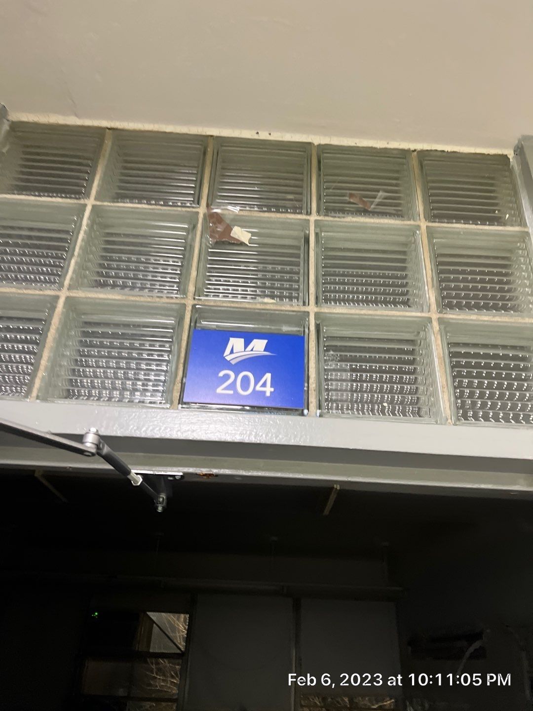A blue sign with the number 204 on it is on a glass block wall.