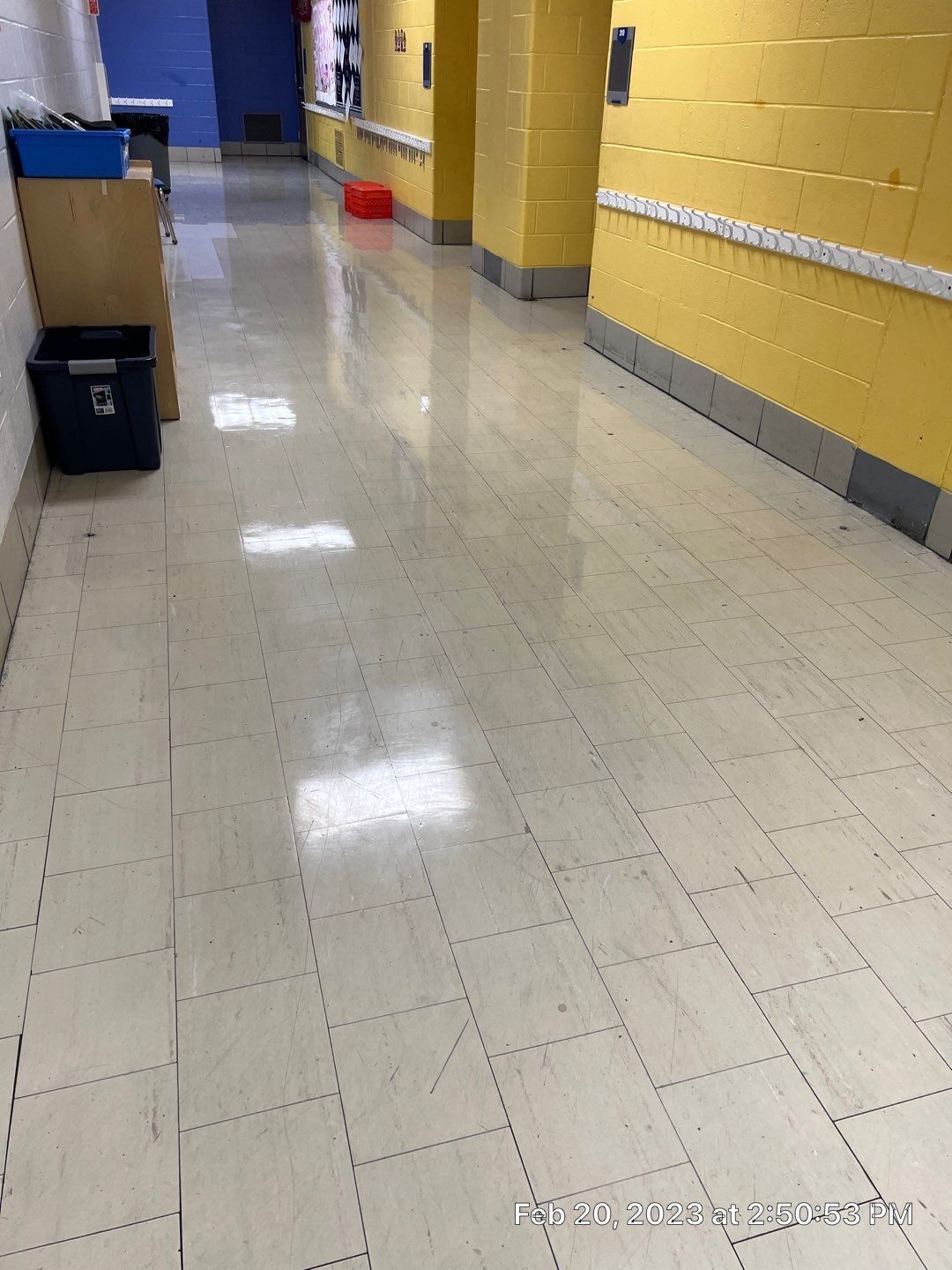 A long hallway with a white tile floor and yellow walls.
