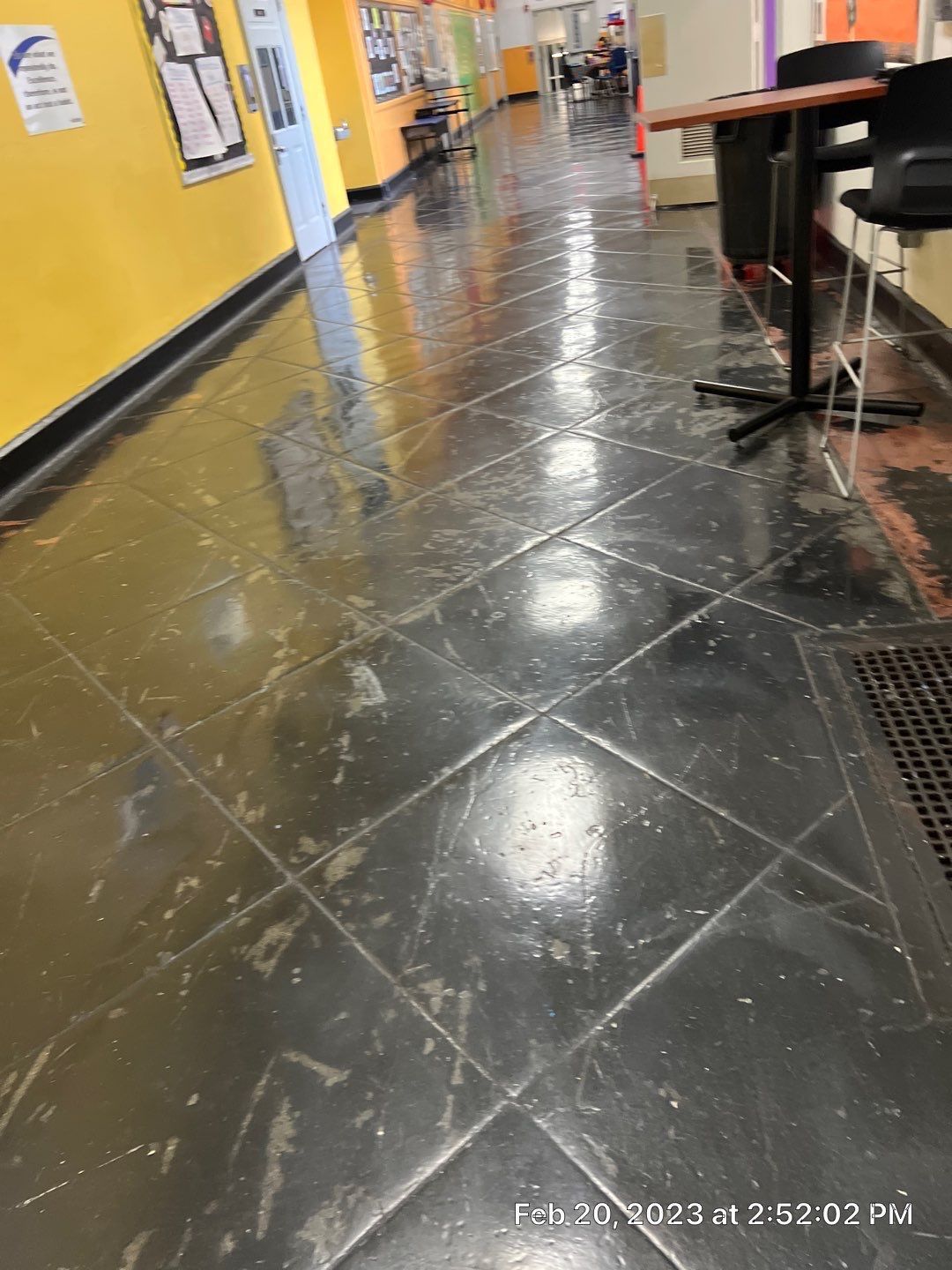 A dirty tiled floor in a hallway with tables and chairs.