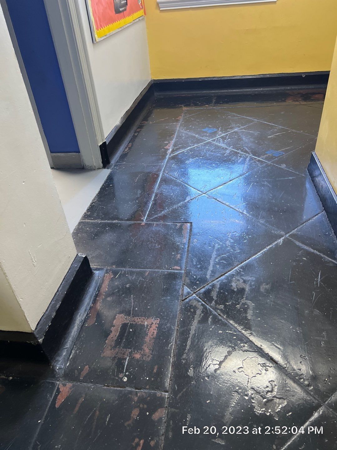 A black tile floor in a hallway with a yellow wall.