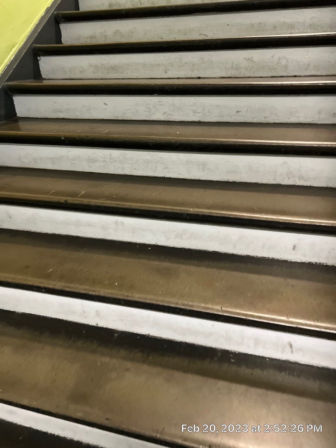 A close up of a set of stairs with a yellow railing.