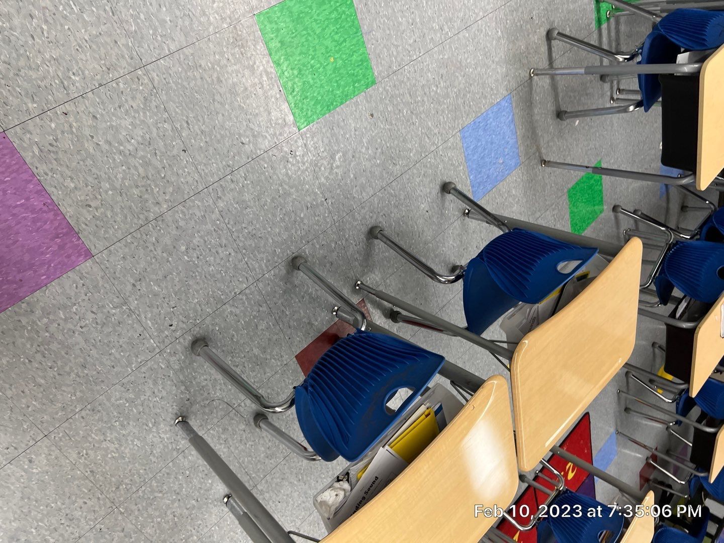 A row of desks and chairs in a classroom with colorful tiles on the floor.