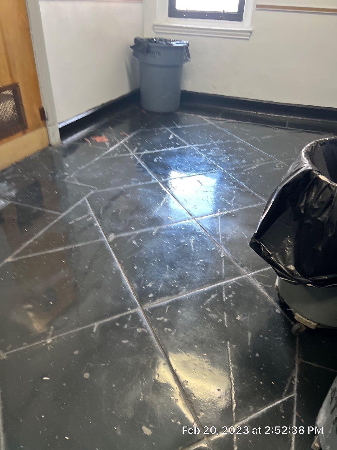 A black tile floor with a trash can in the corner.