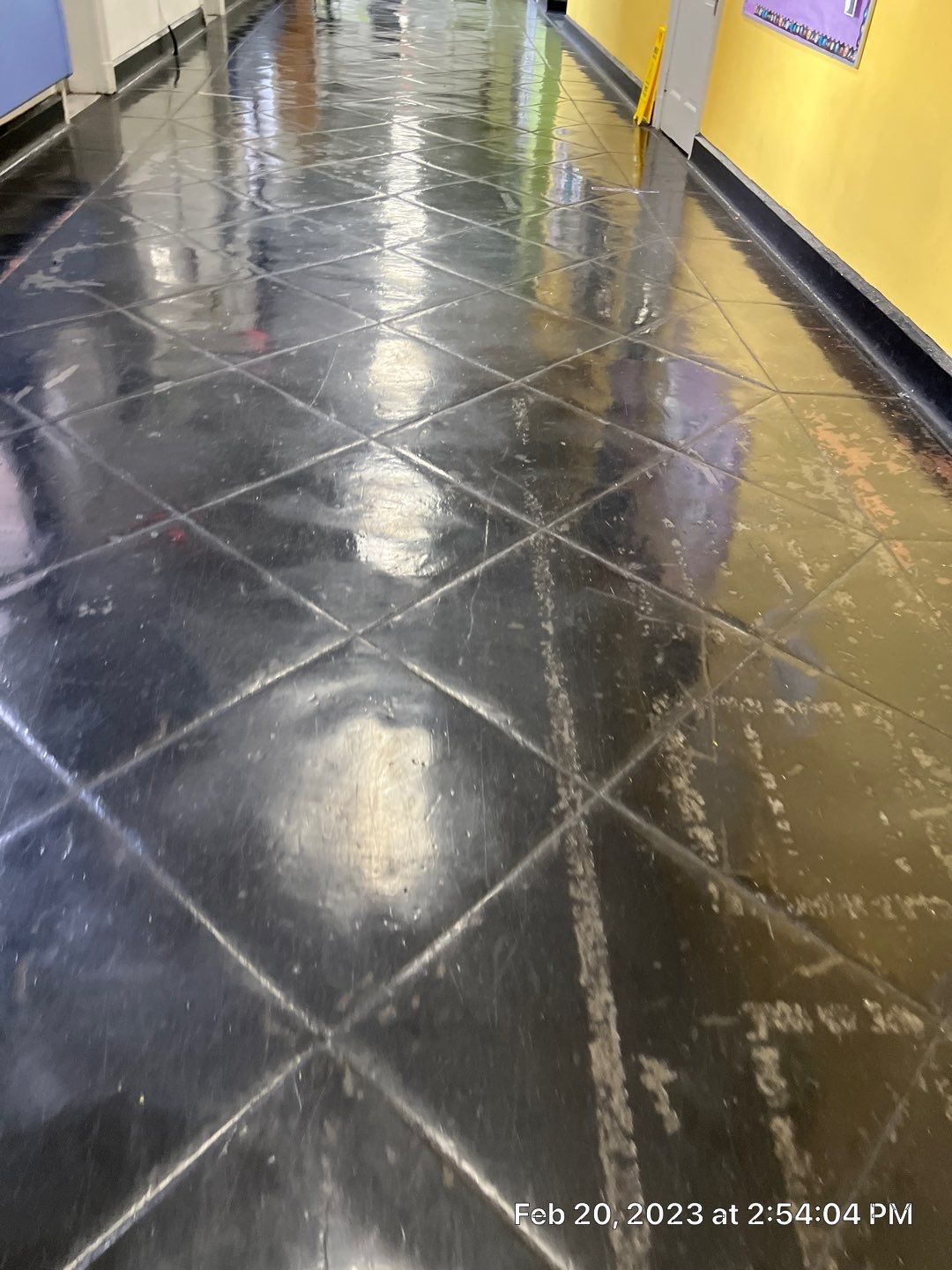 A black tiled floor in a hallway with a yellow wall.