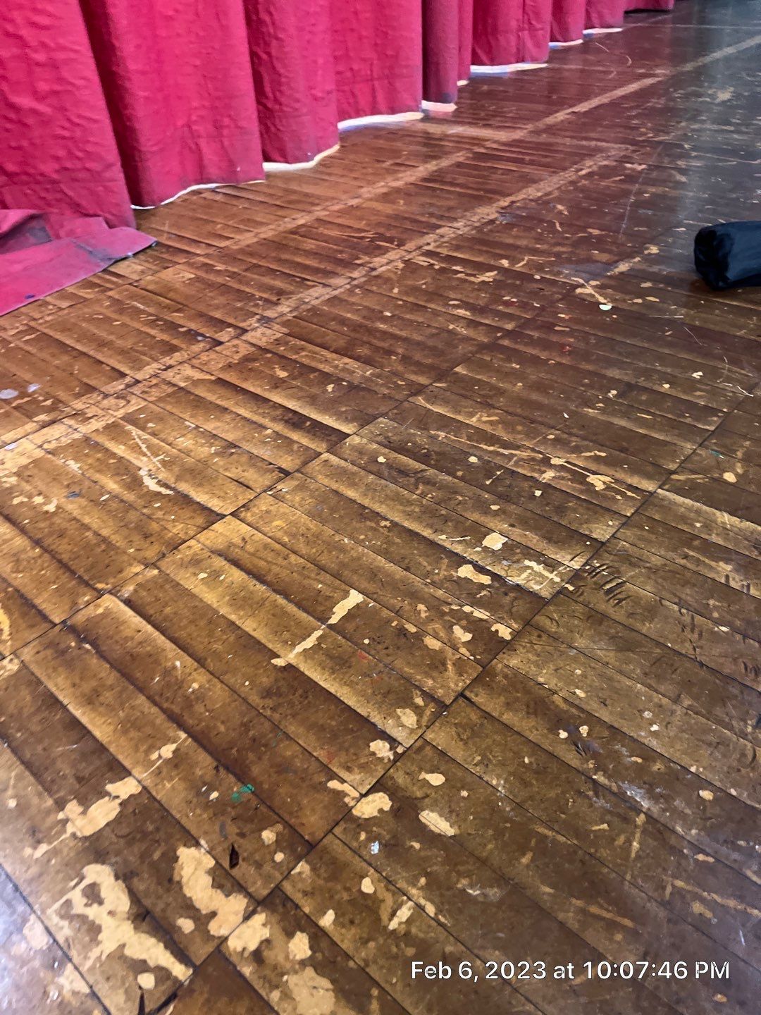 A wooden floor with a red curtain behind it.