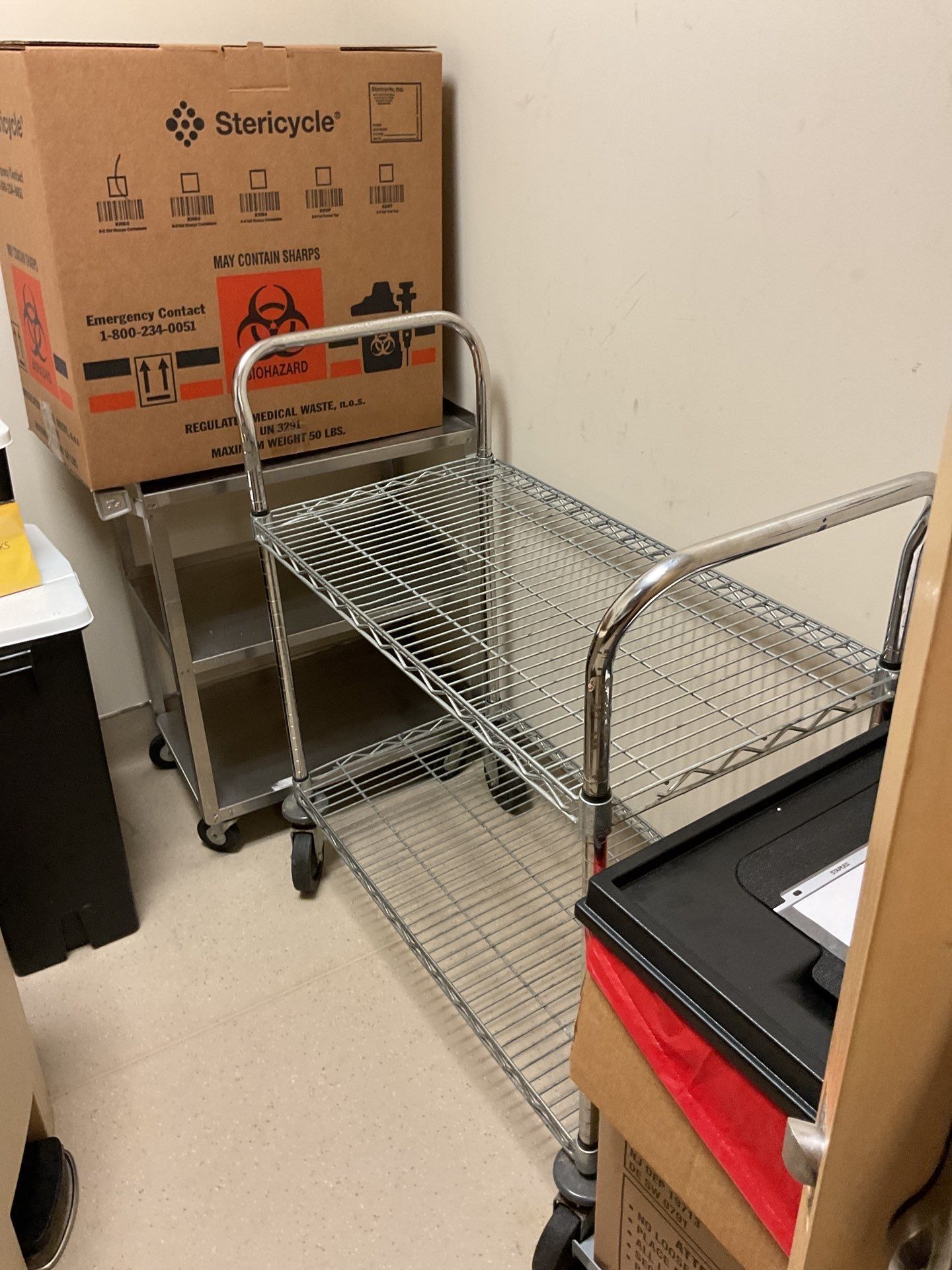Metal carts, storage box with biohazard symbol, and a black container against a beige wall.