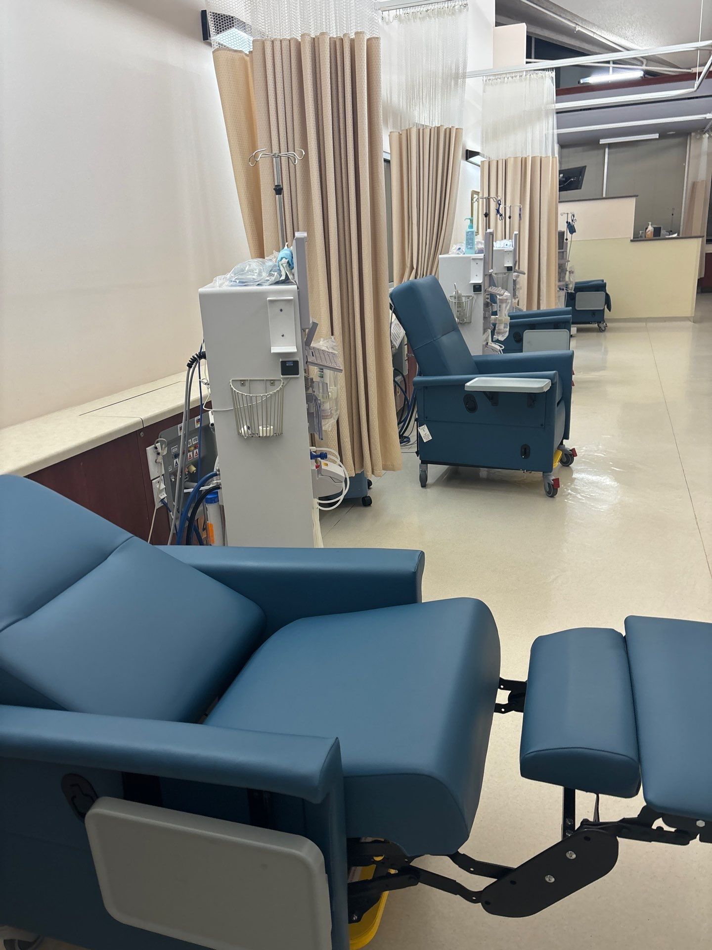 Blue recliners line a medical treatment room with machines and privacy curtains.