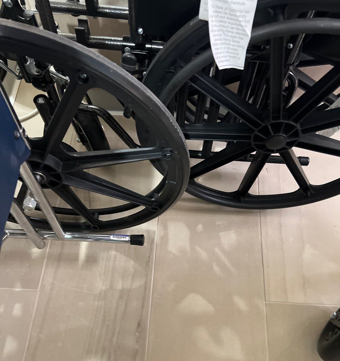 Two black wheelchair wheels on tiled floor. One wheel is close-up, showing its spoke design.
