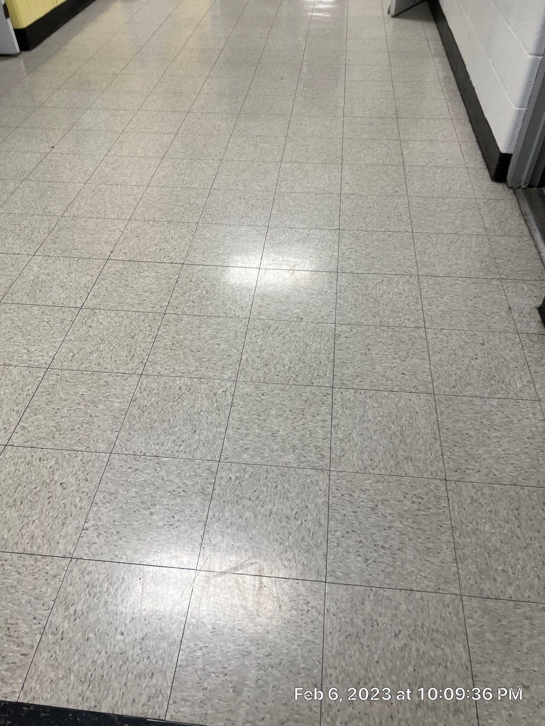 A hallway with a tiled floor and a yellow wall.
