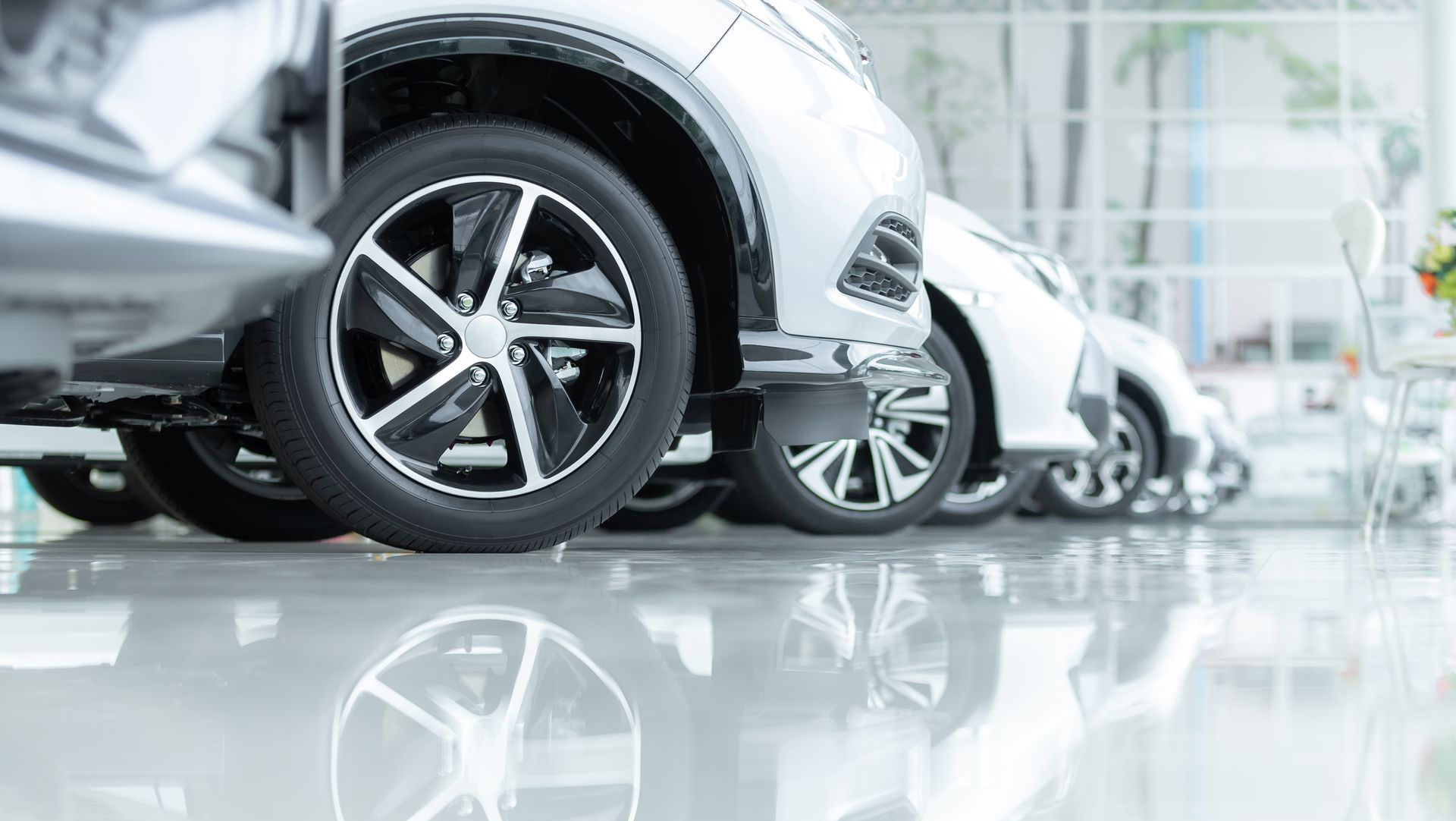 Row of silver cars with shiny tires reflected in a polished floor.