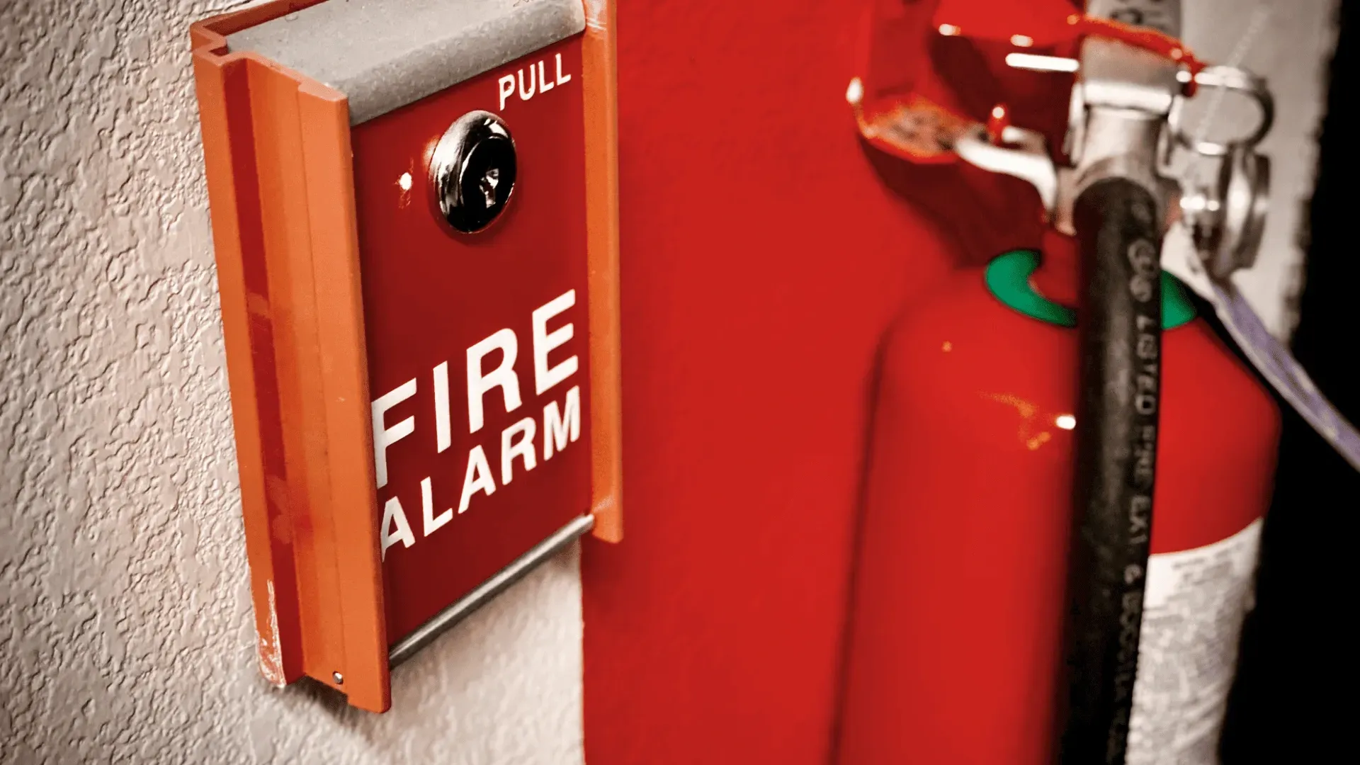 Fire alarm pull station and red fire extinguisher on a wall.