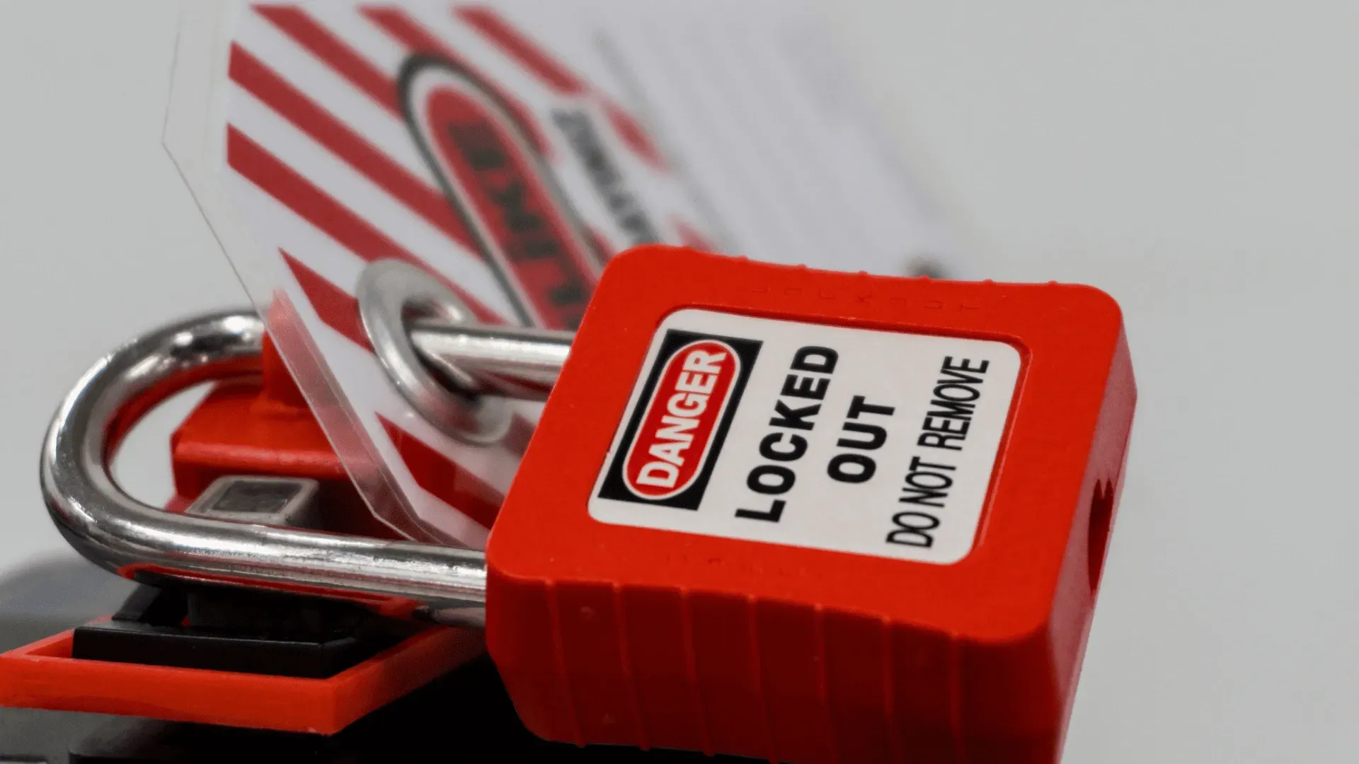 Red lockout padlock with a danger tag, securing a machine, white background.