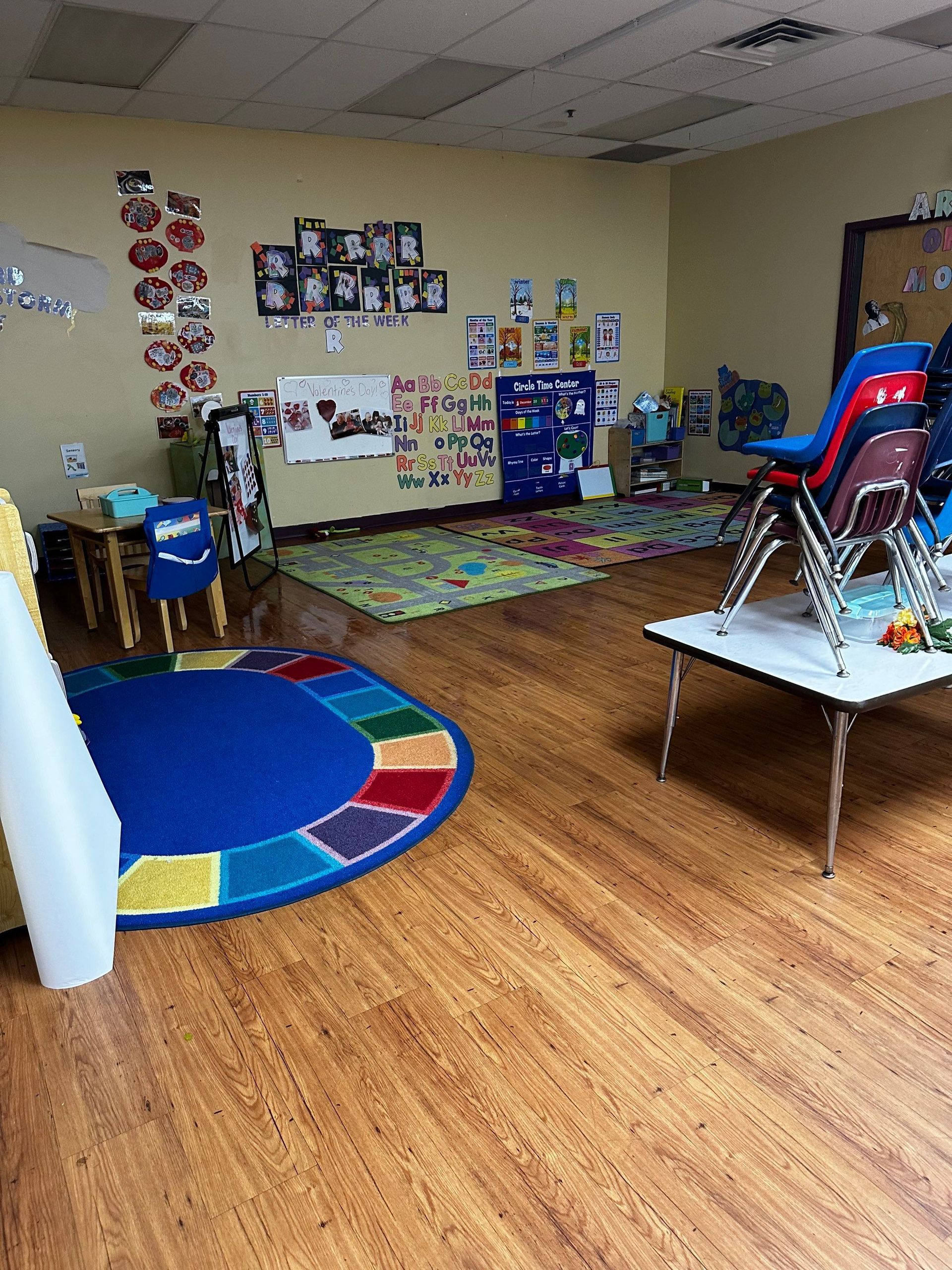 A classroom with wooden floors and a blue rug