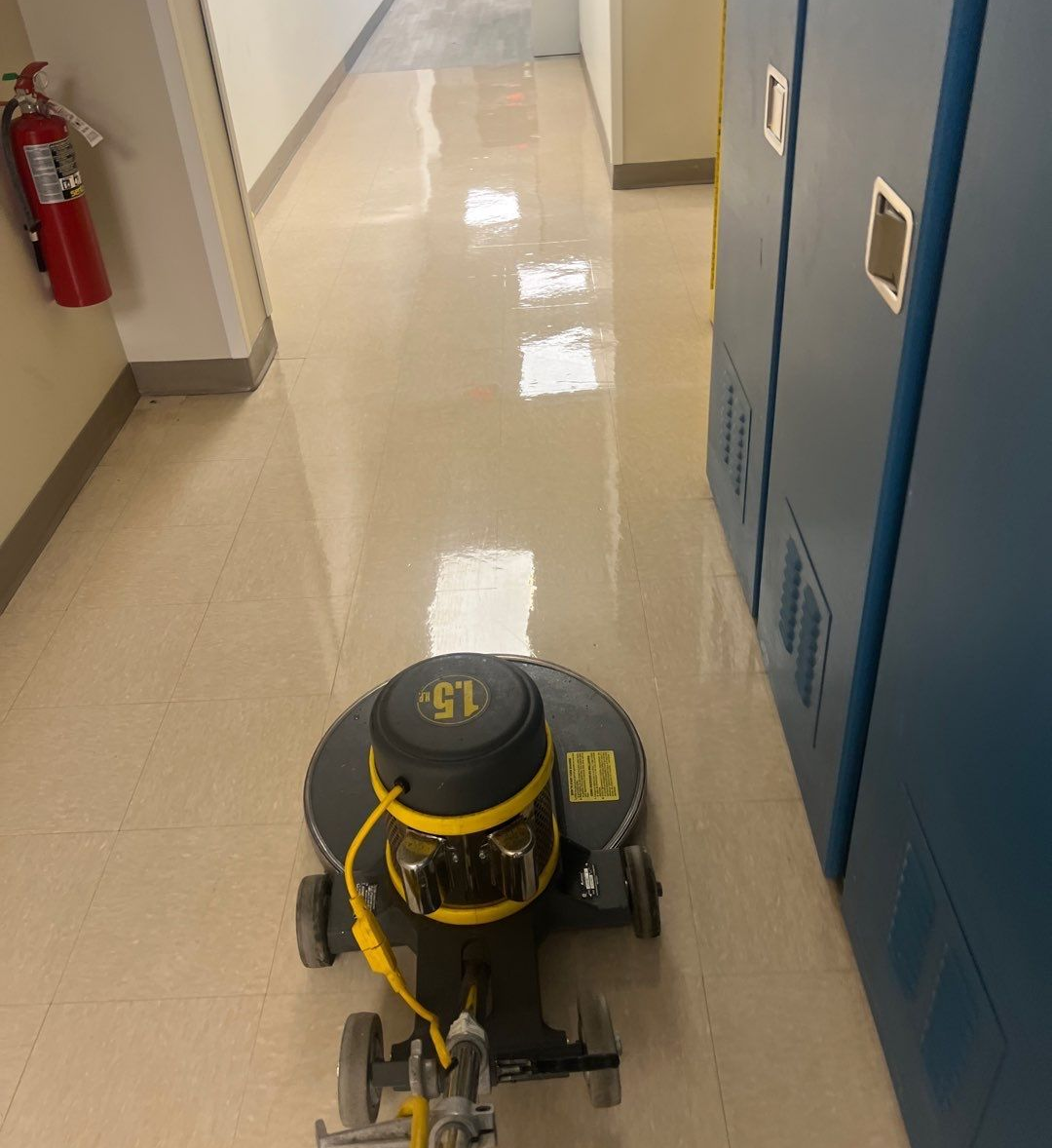 A floor-buffing machine cleaning a hallway with blue storage cabinets.