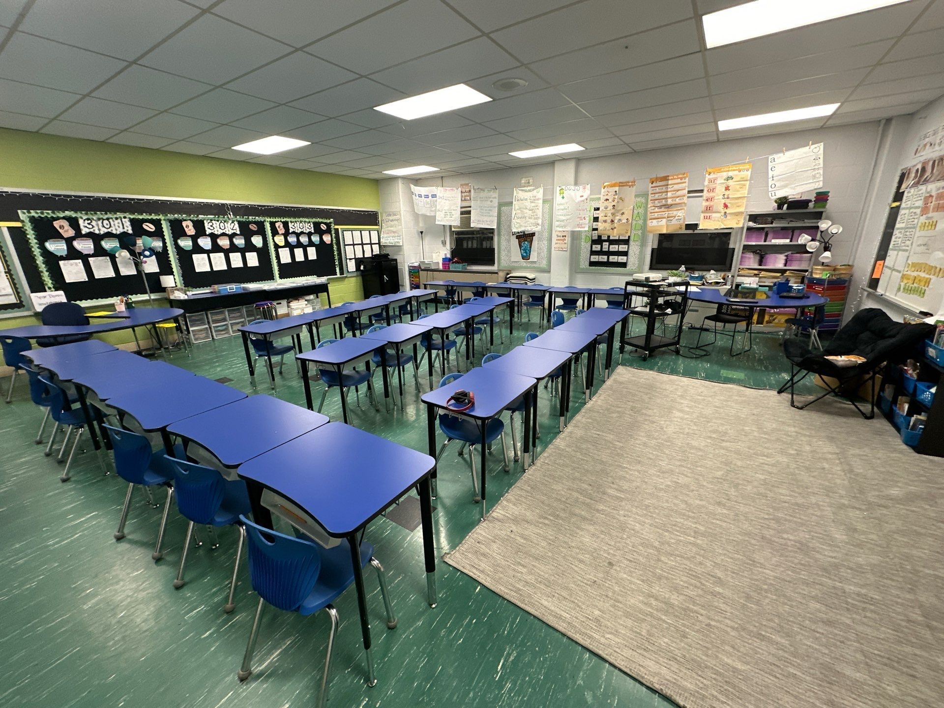 A classroom with blue tables and chairs and a green floor.