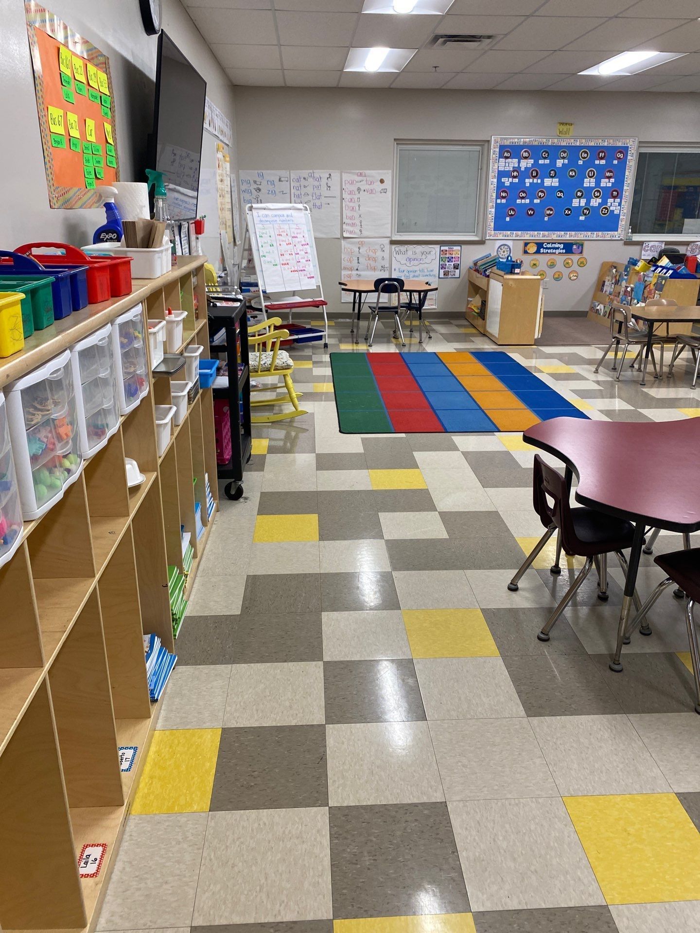 A classroom with tables and chairs and a colorful rug on the floor.