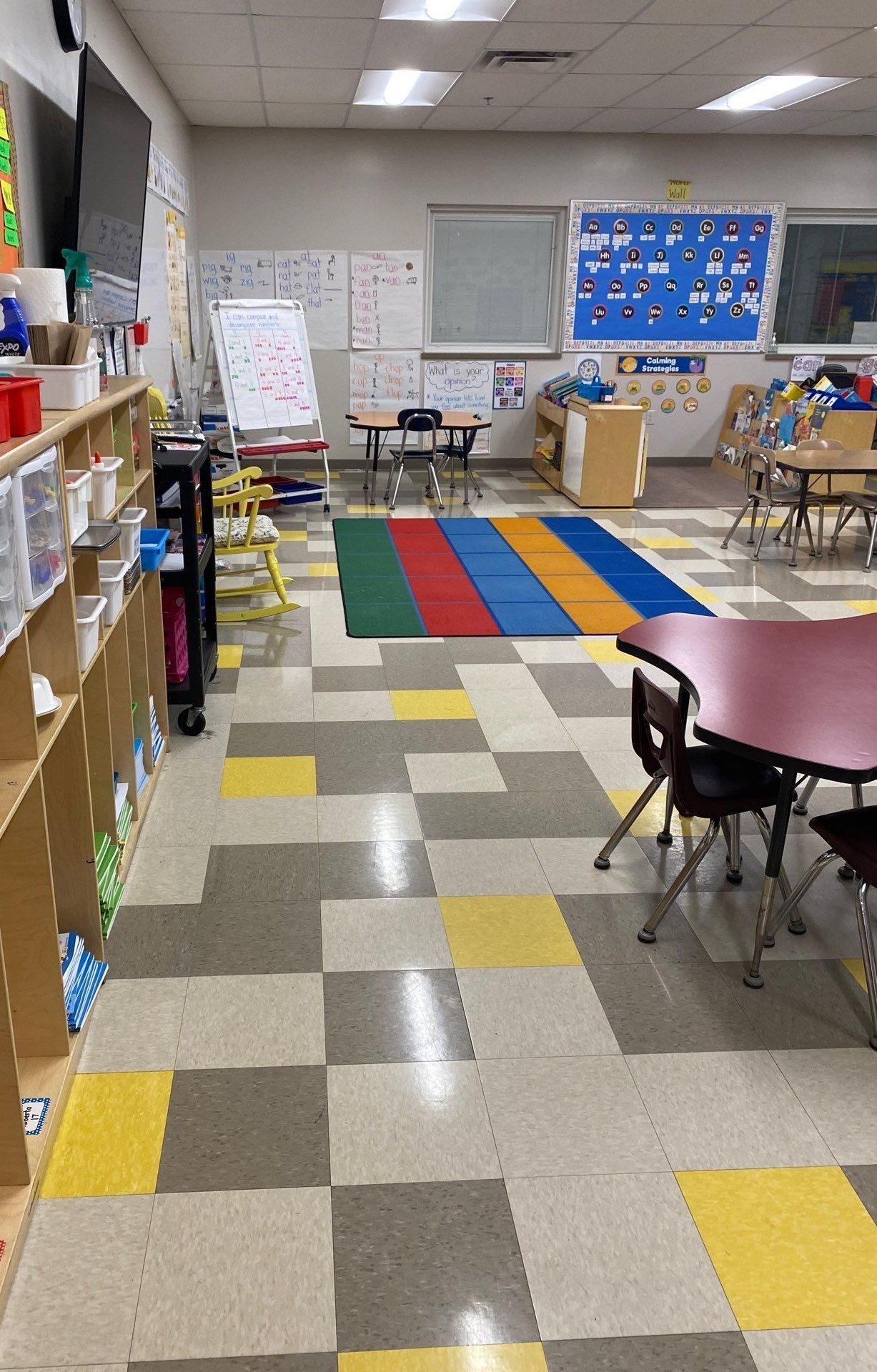 Classroom with shelves of bins, tables, and colorful floor mats.