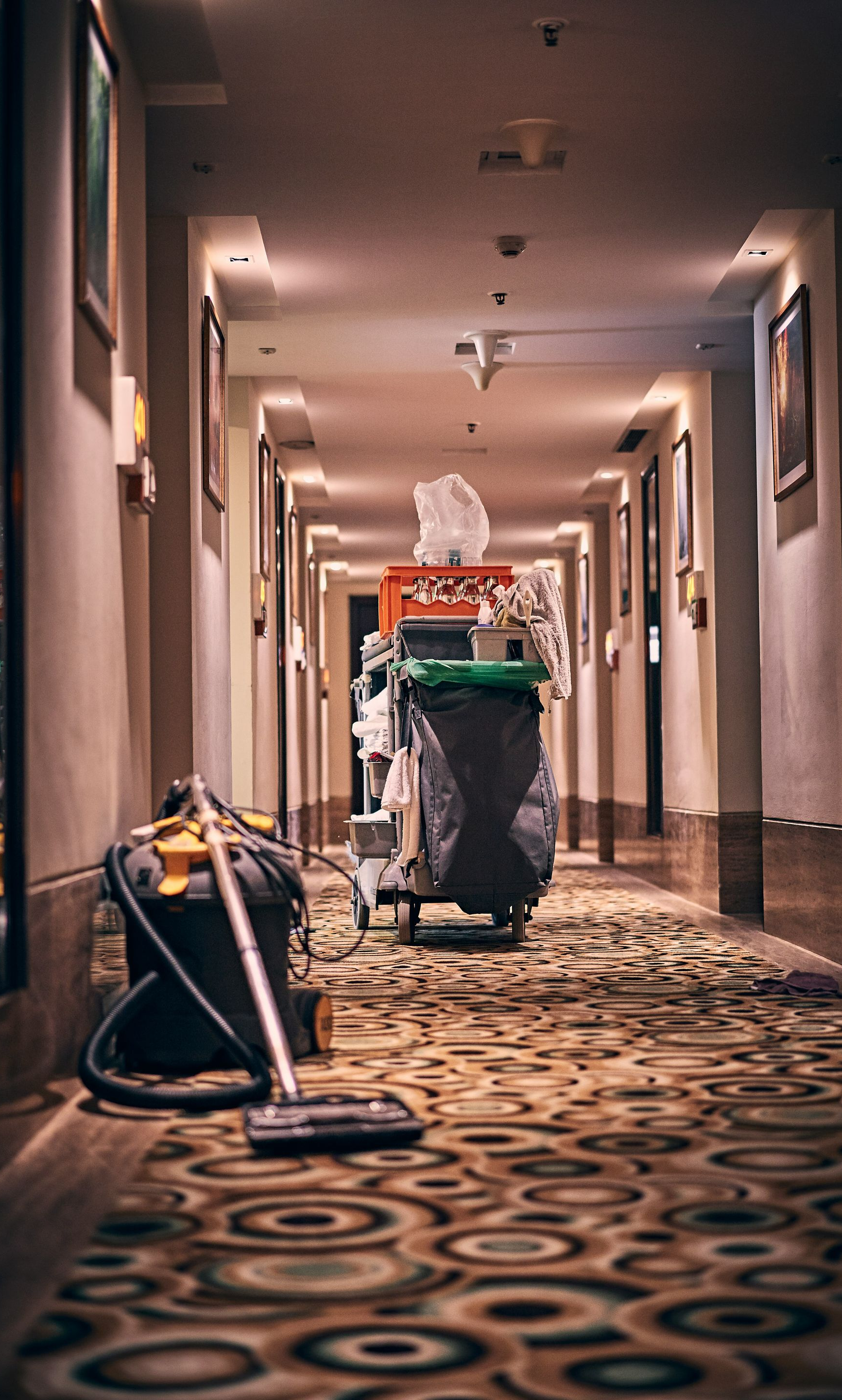 Hotel hallway with cleaning cart and vacuum cleaner.