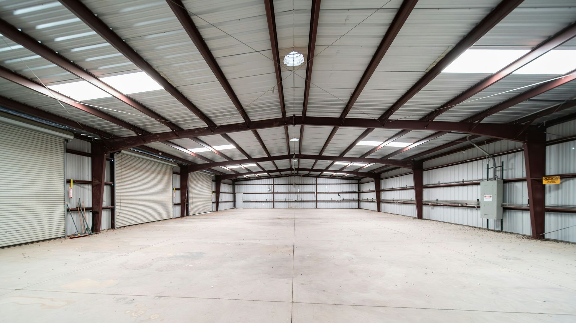 Empty warehouse interior, steel framework, concrete floor, overhead lights, and white walls.