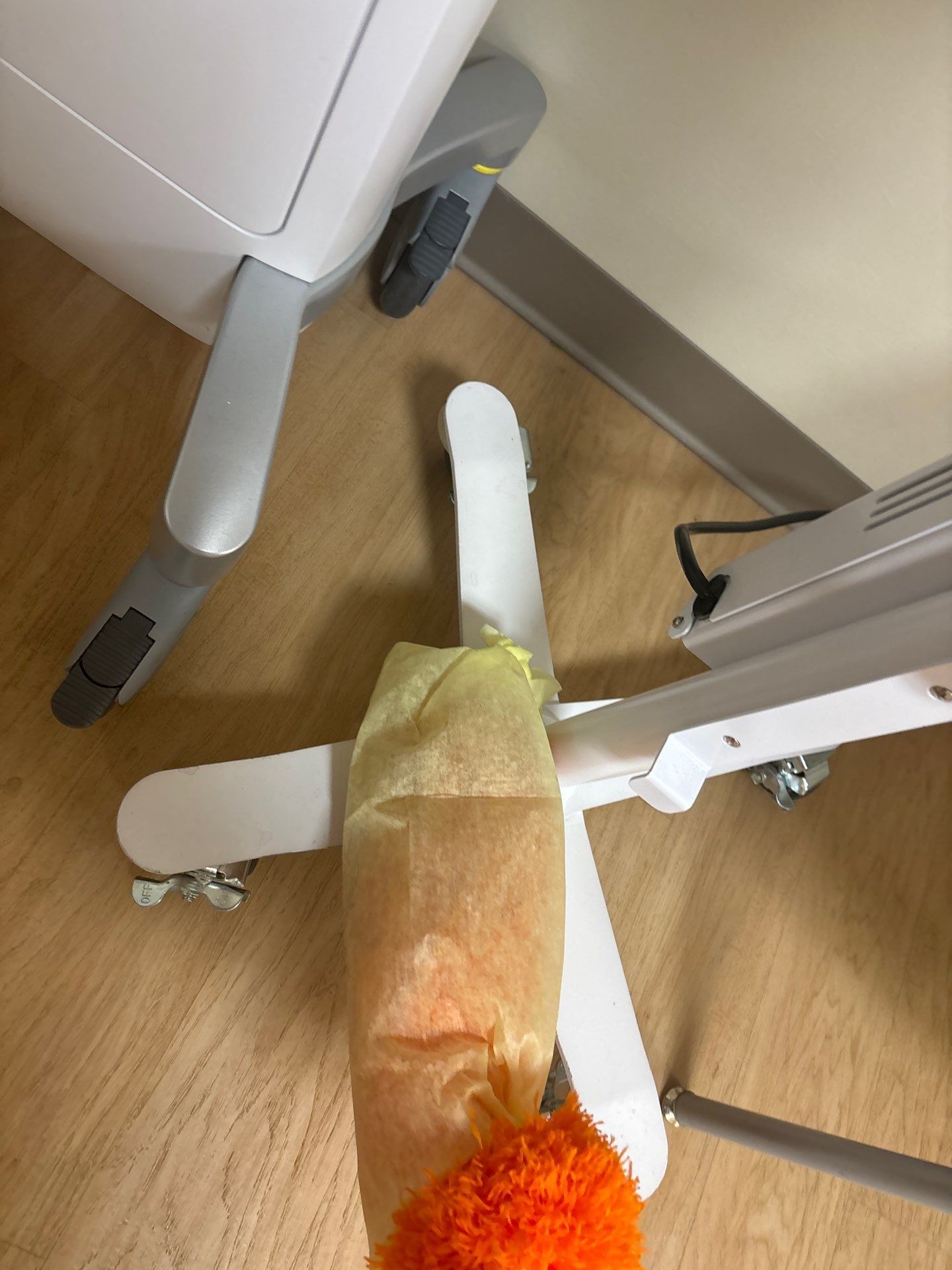 White medical equipment with a wrapped item and orange cleaning brush on a light wood floor.