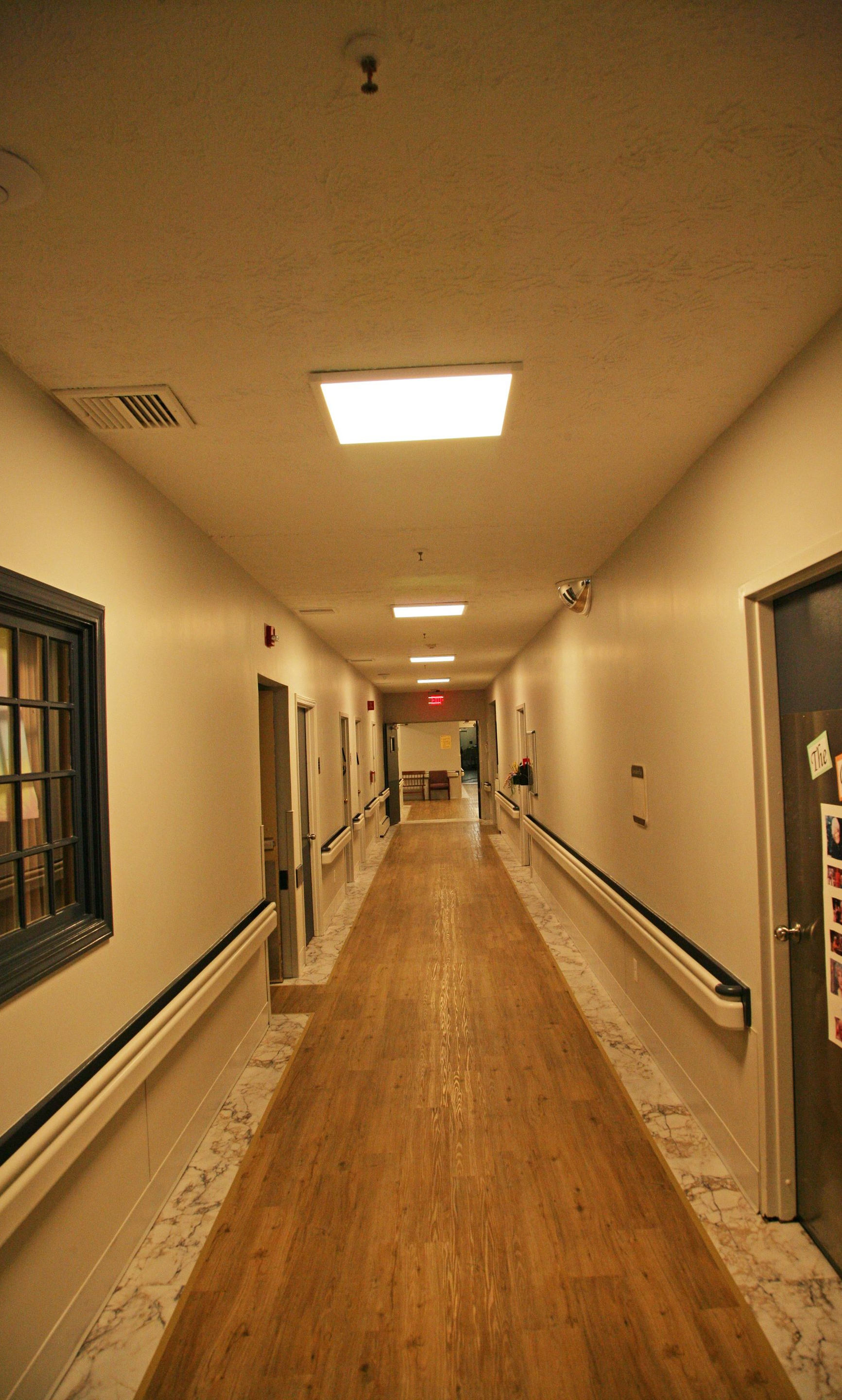 Long, brightly lit hallway with wooden floor, white walls, and doors along the sides.
