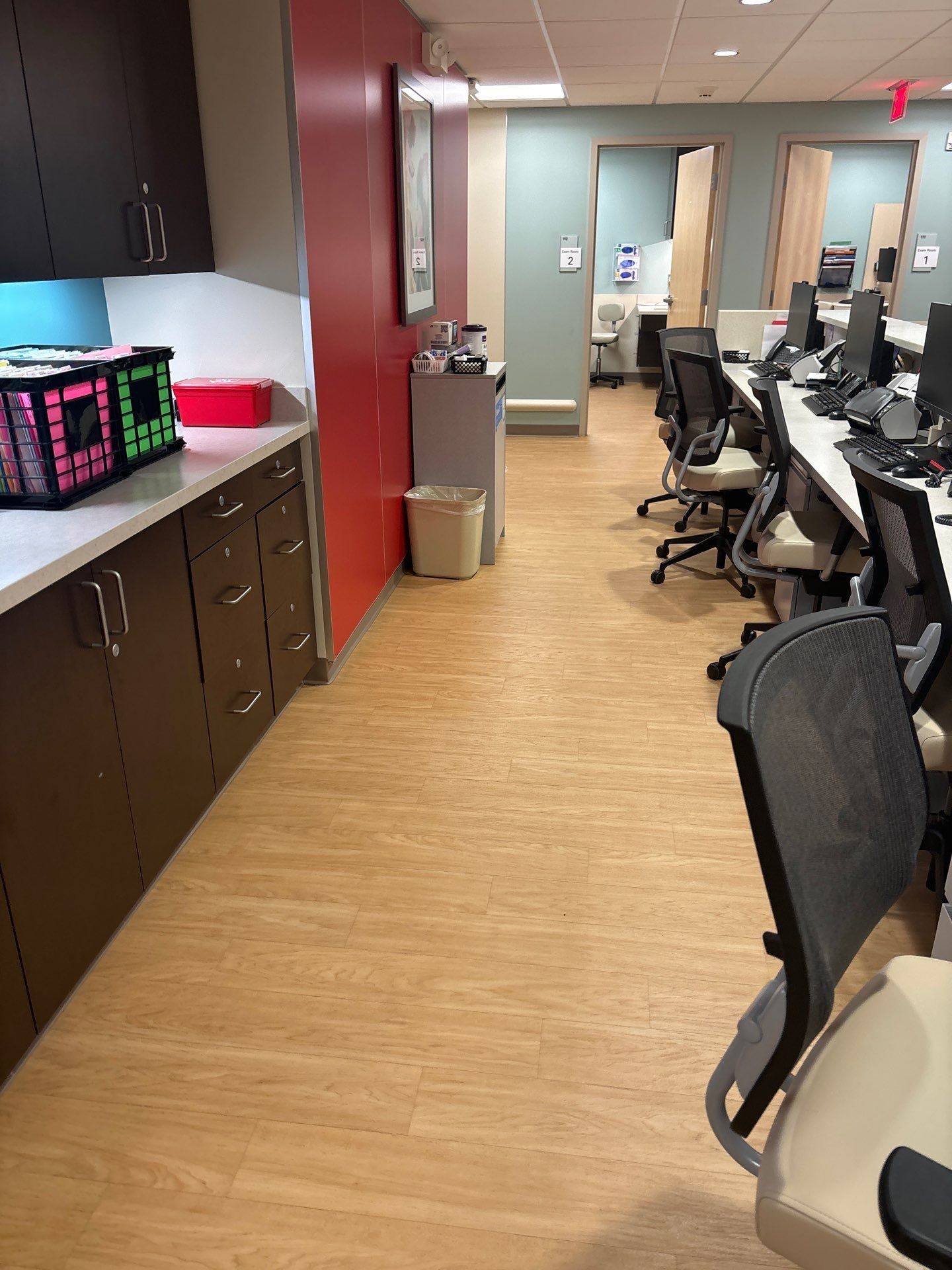 A medical office hallway with workstations, cabinets, and a red accent wall.