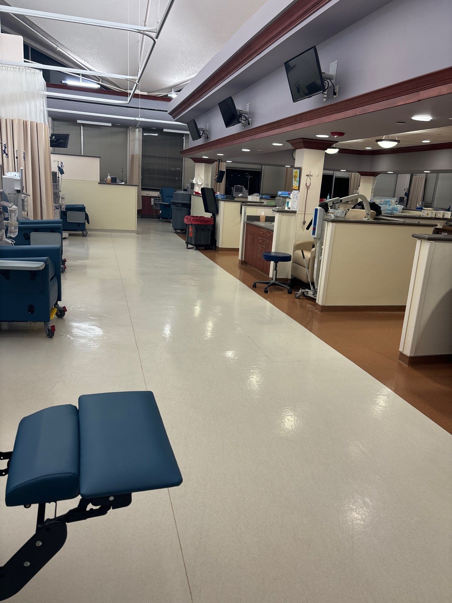 An empty medical treatment room with blue chairs, workstations, and overhead monitors. White and brown interior.