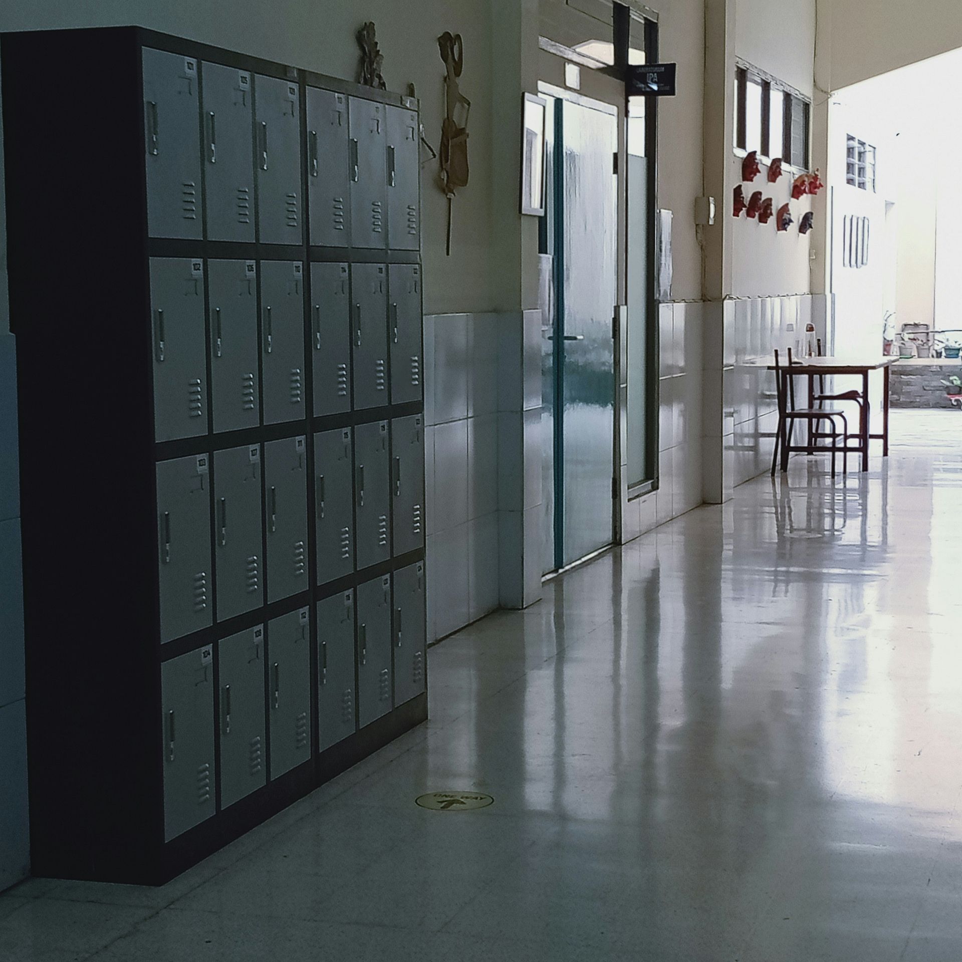 School hallway with metal lockers on one side and reflective flooring.