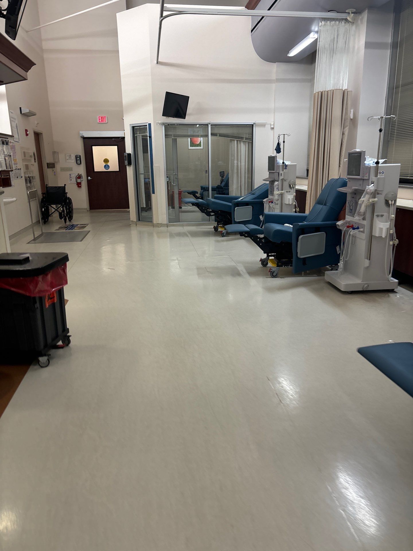 Interior of a dialysis clinic with reclining chairs, medical equipment, and a red biohazard container on wheels.