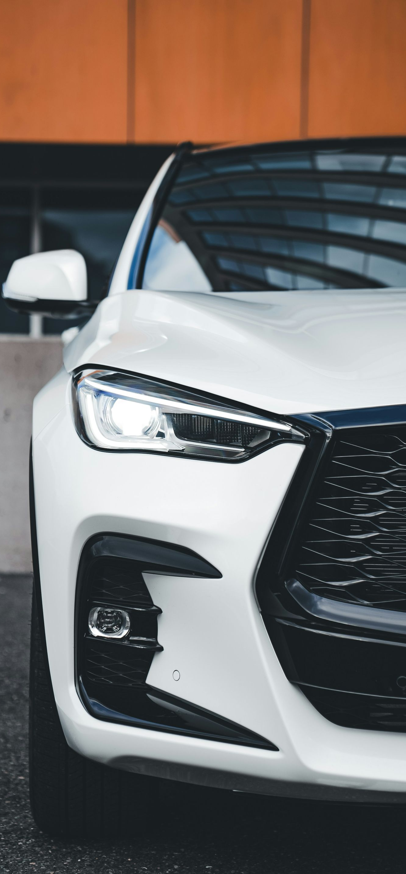 White SUV, partially in view, with black grille and headlights. Outdoors, modern building backdrop.