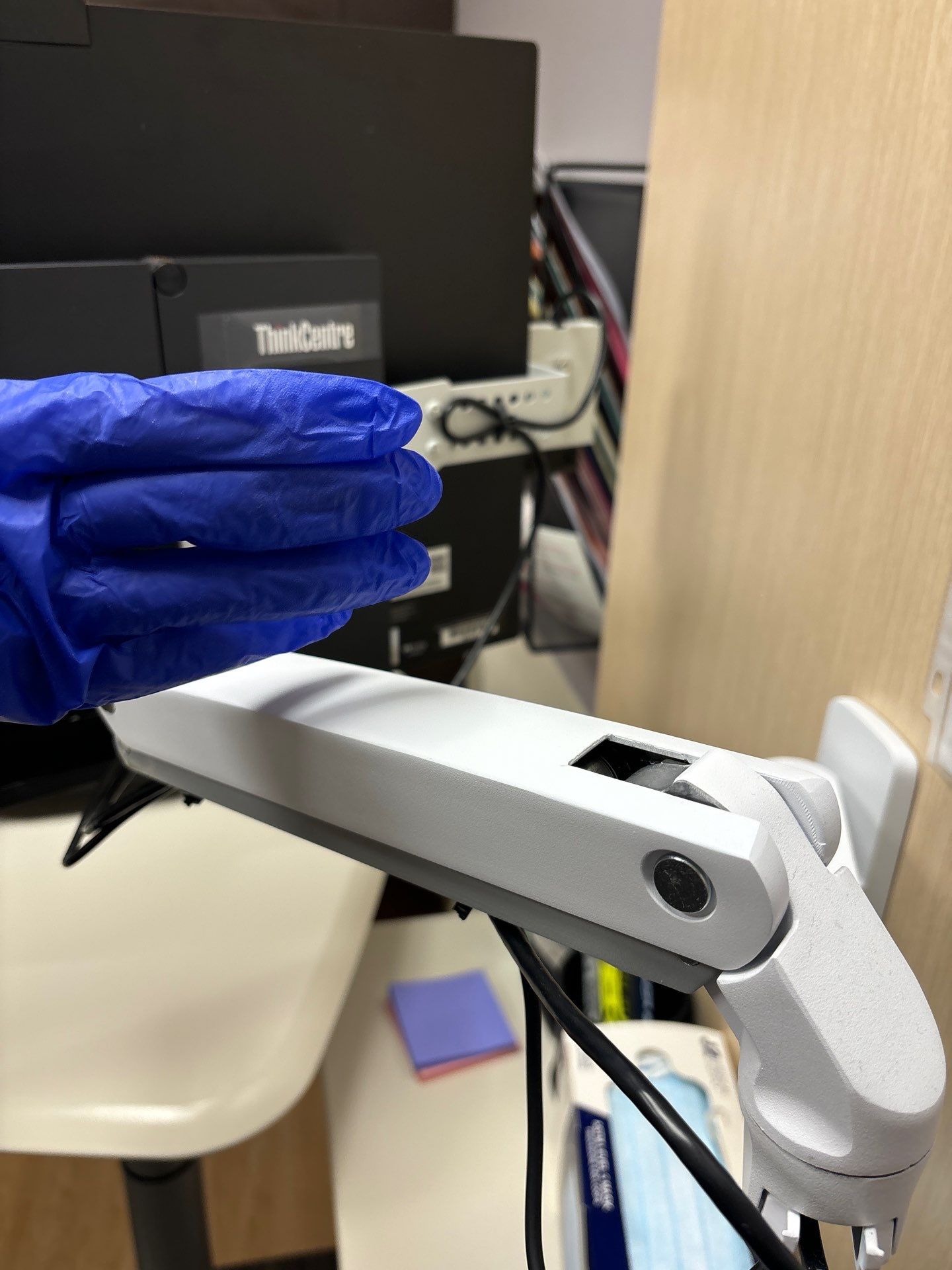 Blue gloved hand over a white projector arm with a computer in the background.