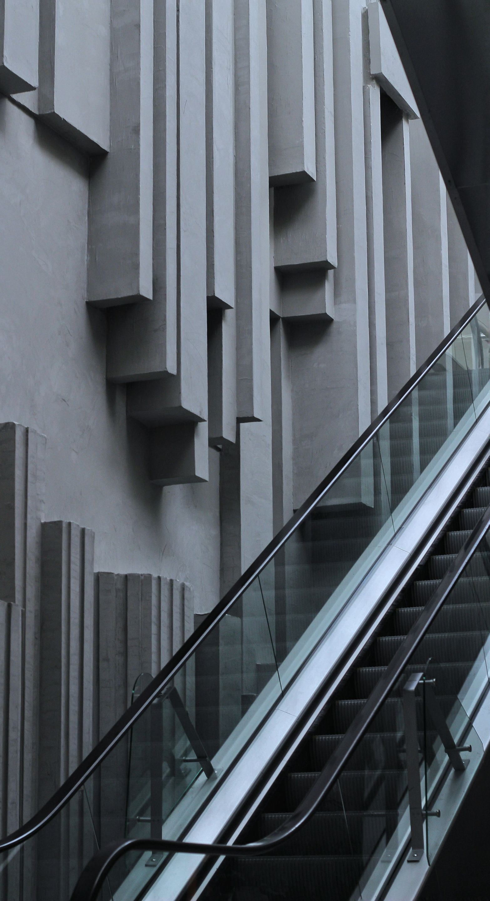 Escalator next to a concrete wall with vertical rectangular protrusions.