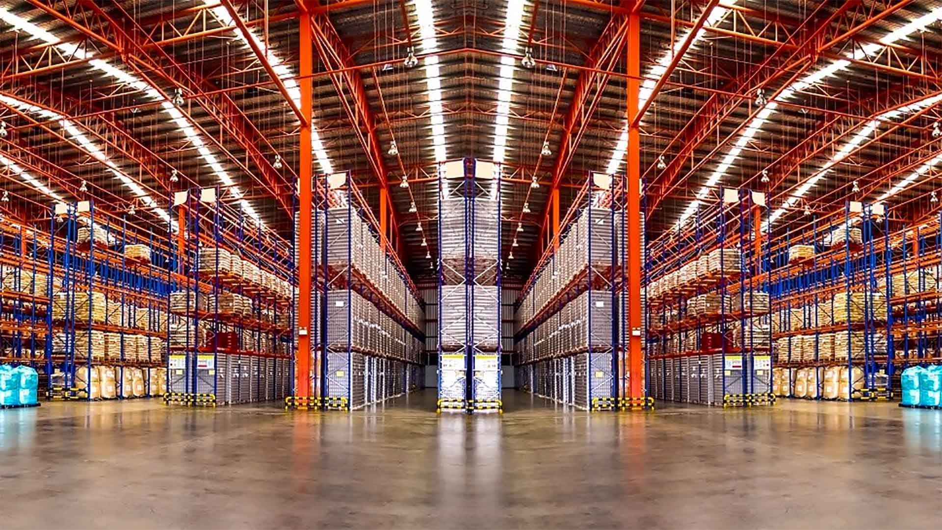 Large, symmetrical warehouse interior with high ceilings, orange steel beams, and tall shelves filled with inventory.