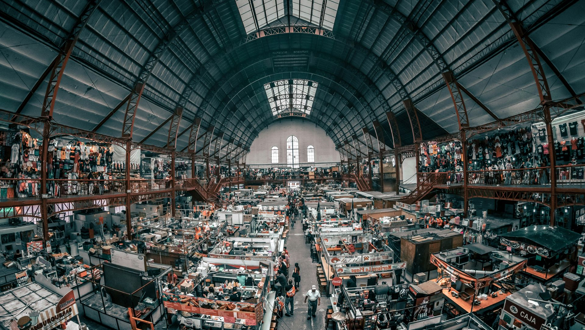 Large, bustling market inside a high-ceilinged building with many stalls and people shopping.