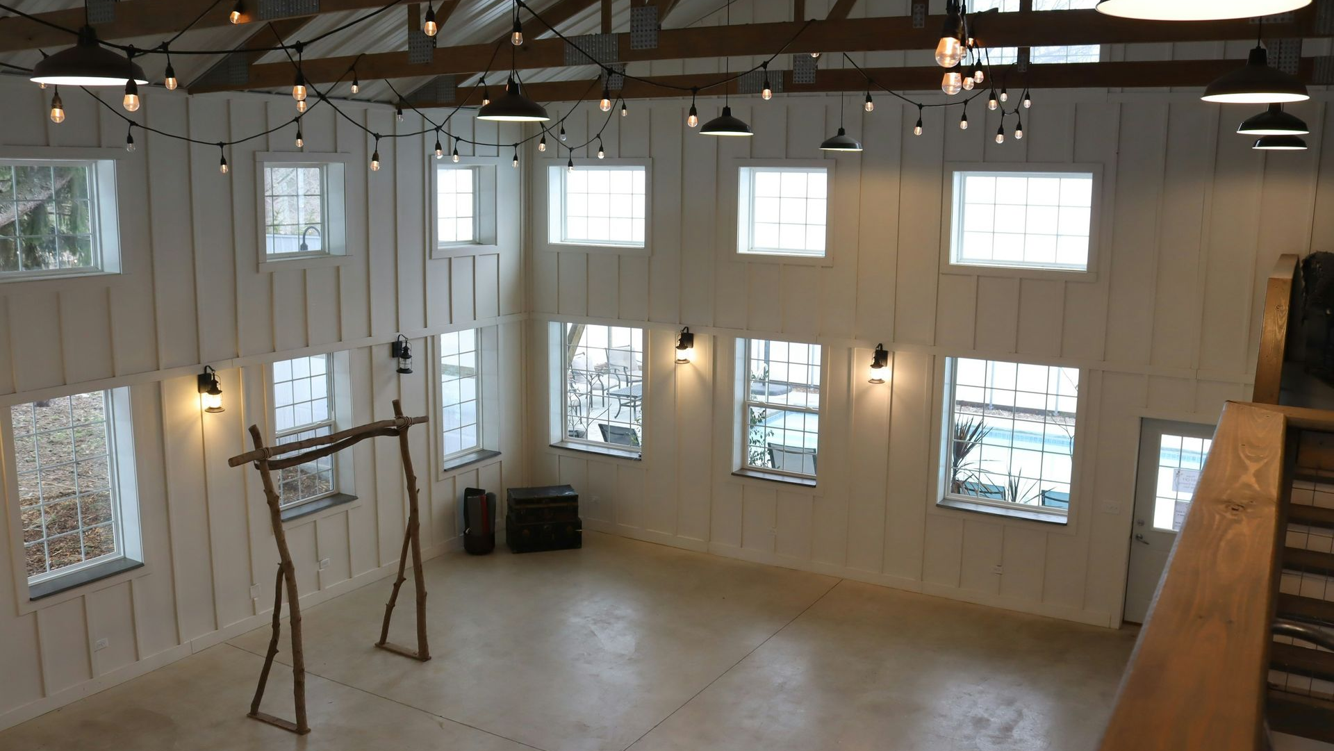 A bright, airy event space with white board-and-batten walls, hanging industrial lights, and large windows.