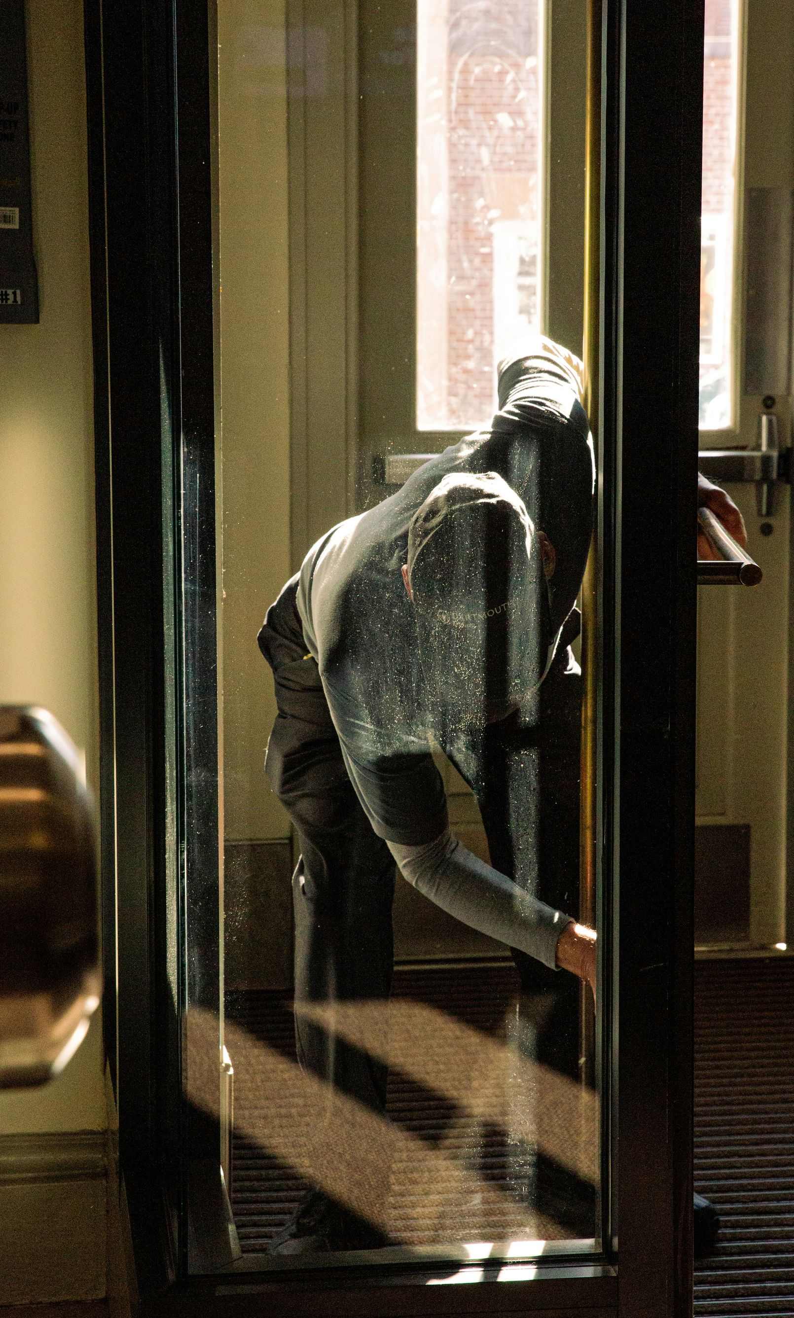 Person in a sparkly shirt, leaning to the side, reaching towards a glass door with sunlight streaming through.