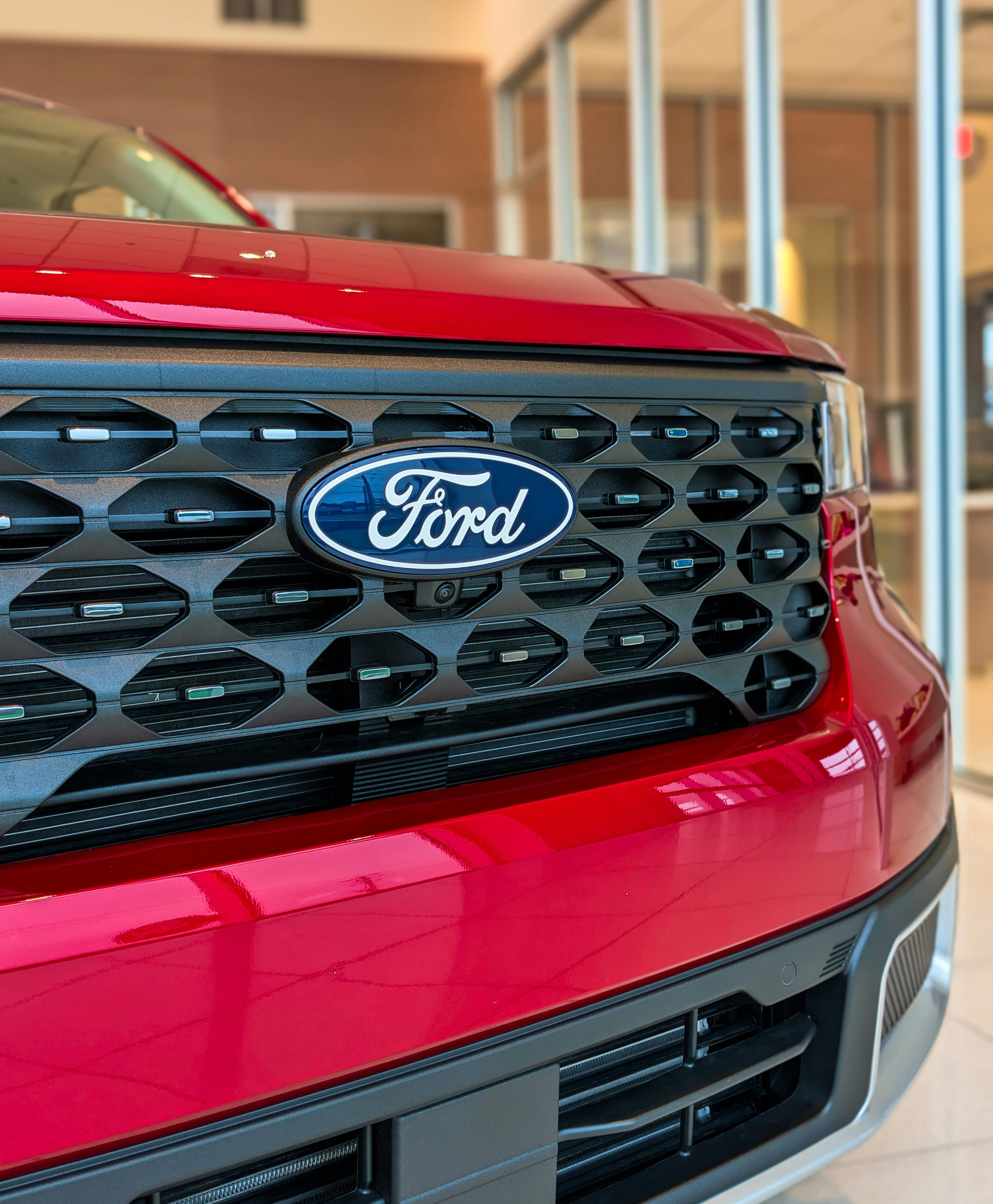 Red Ford SUV grille with blue Ford emblem in a showroom.