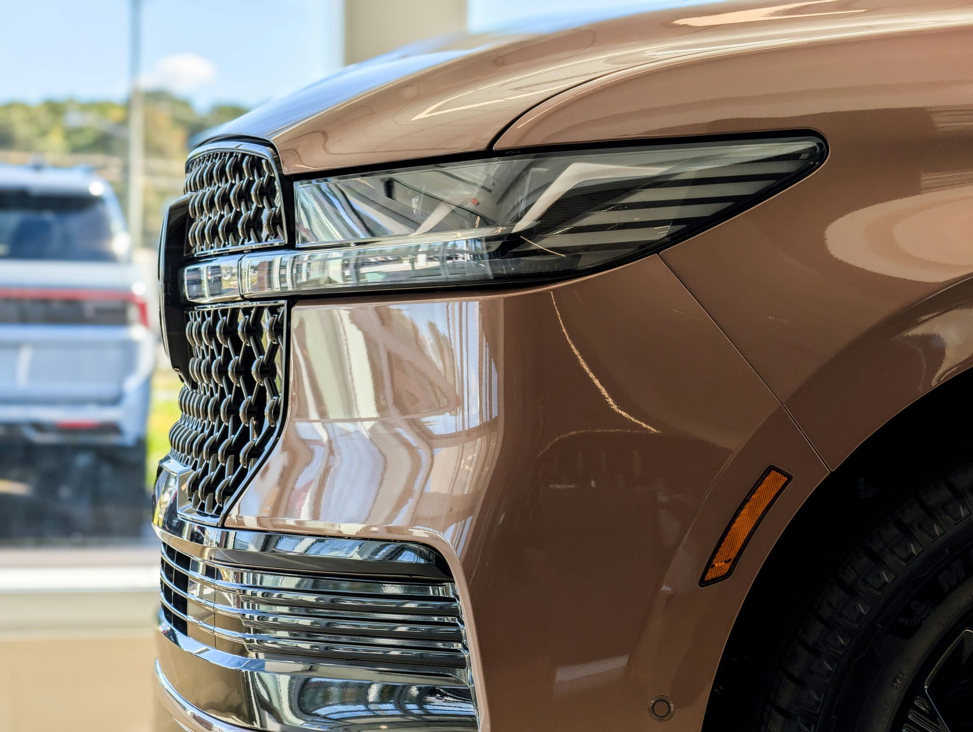 Close-up of a bronze luxury SUV's front grille, sharp LED headlight, and amber side marker light.