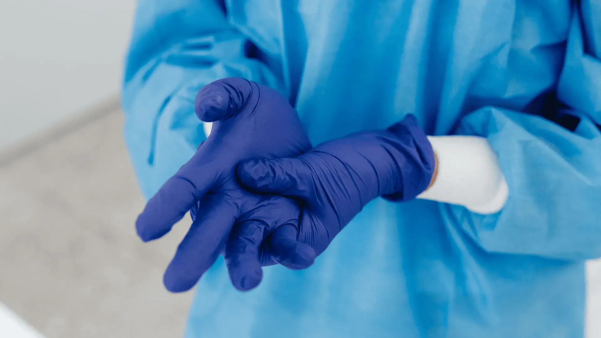 Person wearing blue medical gloves and a blue gown.