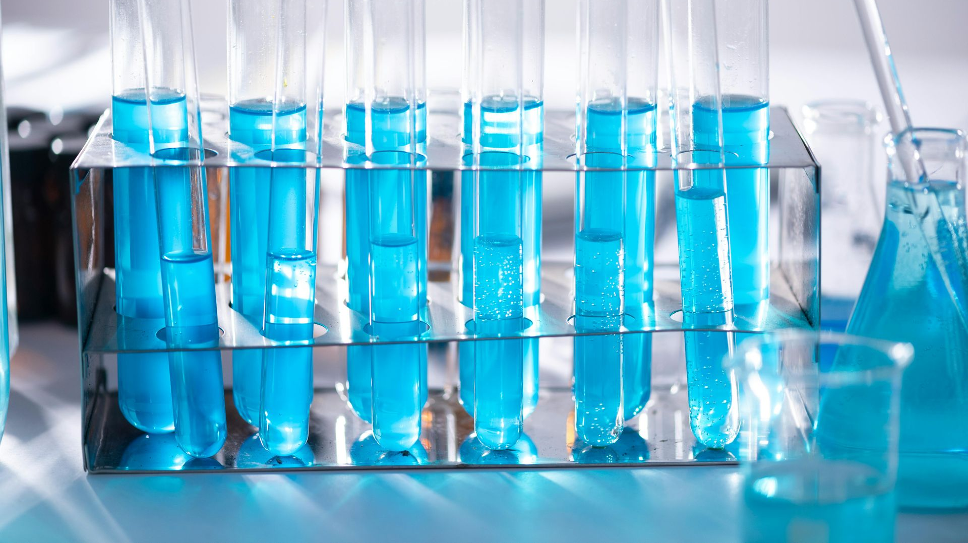 Test tubes with blue liquid in a rack, beakers and flasks in a lab setting.