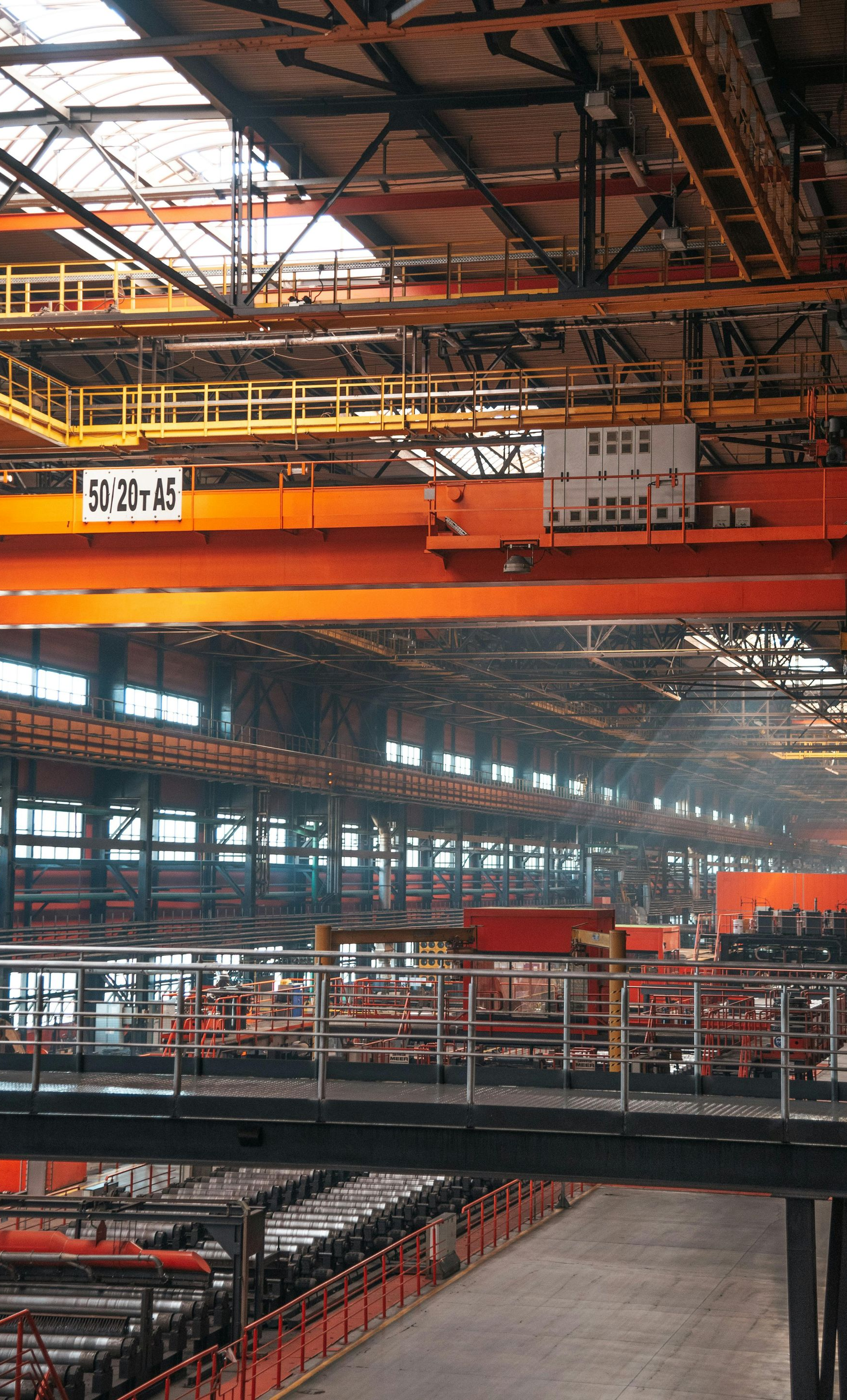 Large industrial factory interior featuring heavy orange overhead cranes, metal walkways, and vast workshop floor space.