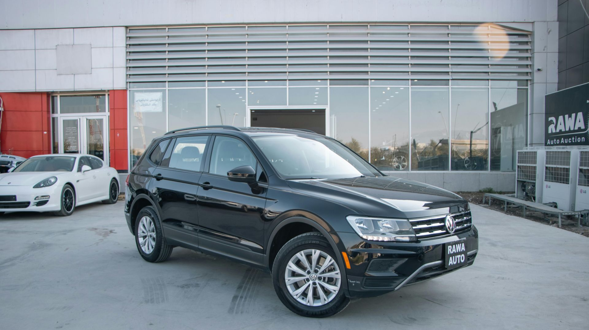Black Volkswagen Tiguan SUV parked in front of a car dealership on a sunny day.