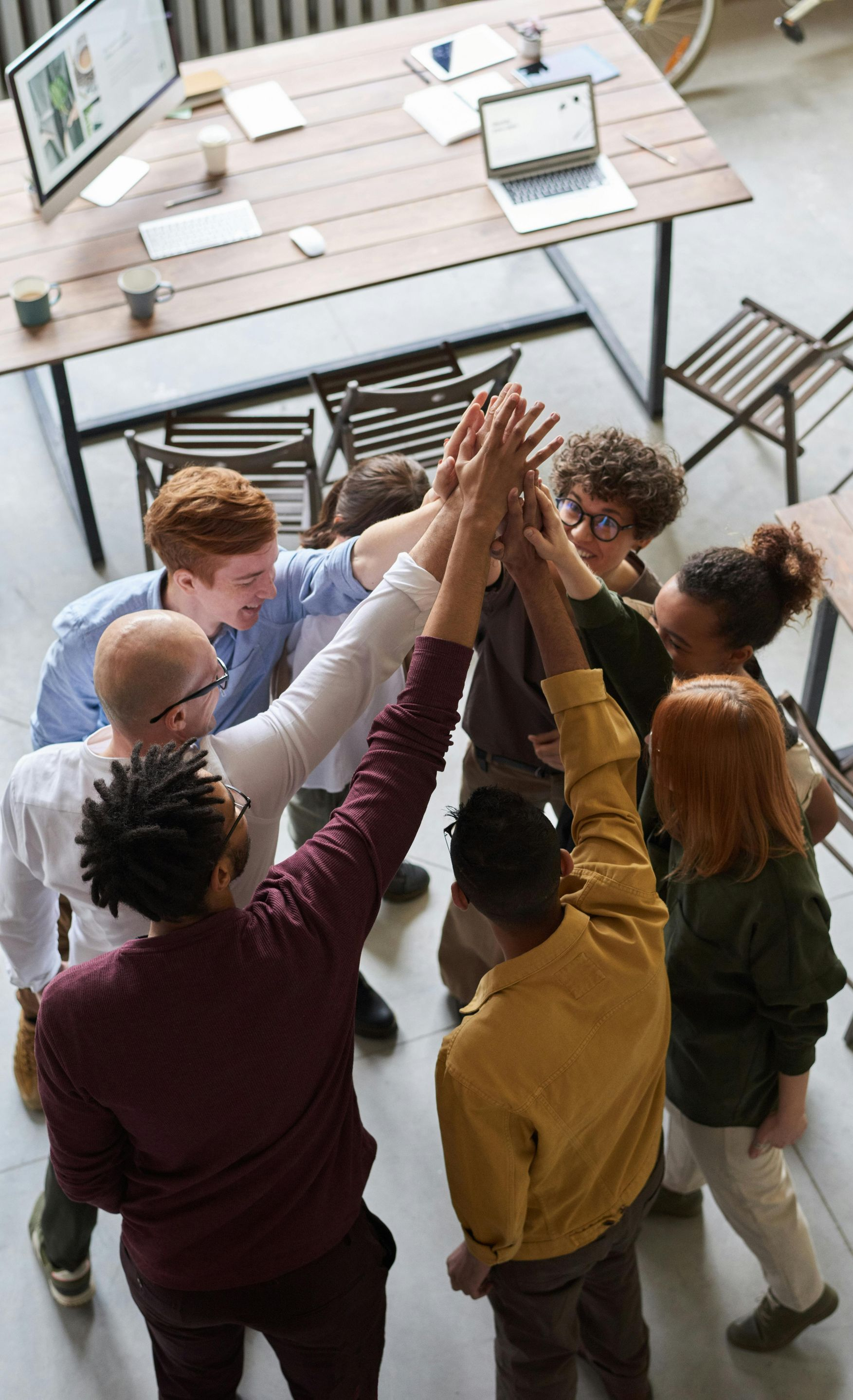 Group of diverse people in a circle, hands raised in a high five in an office setting.