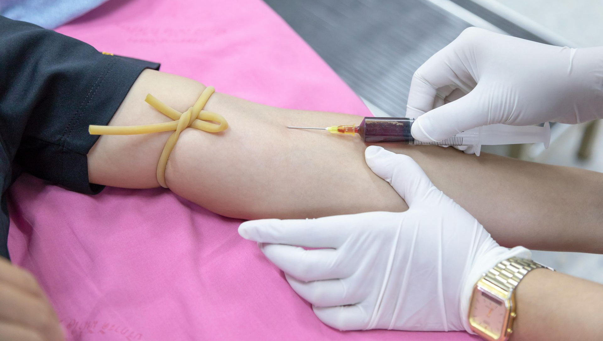 Person's arm with tourniquet, being injected with a needle for blood draw in a medical setting.