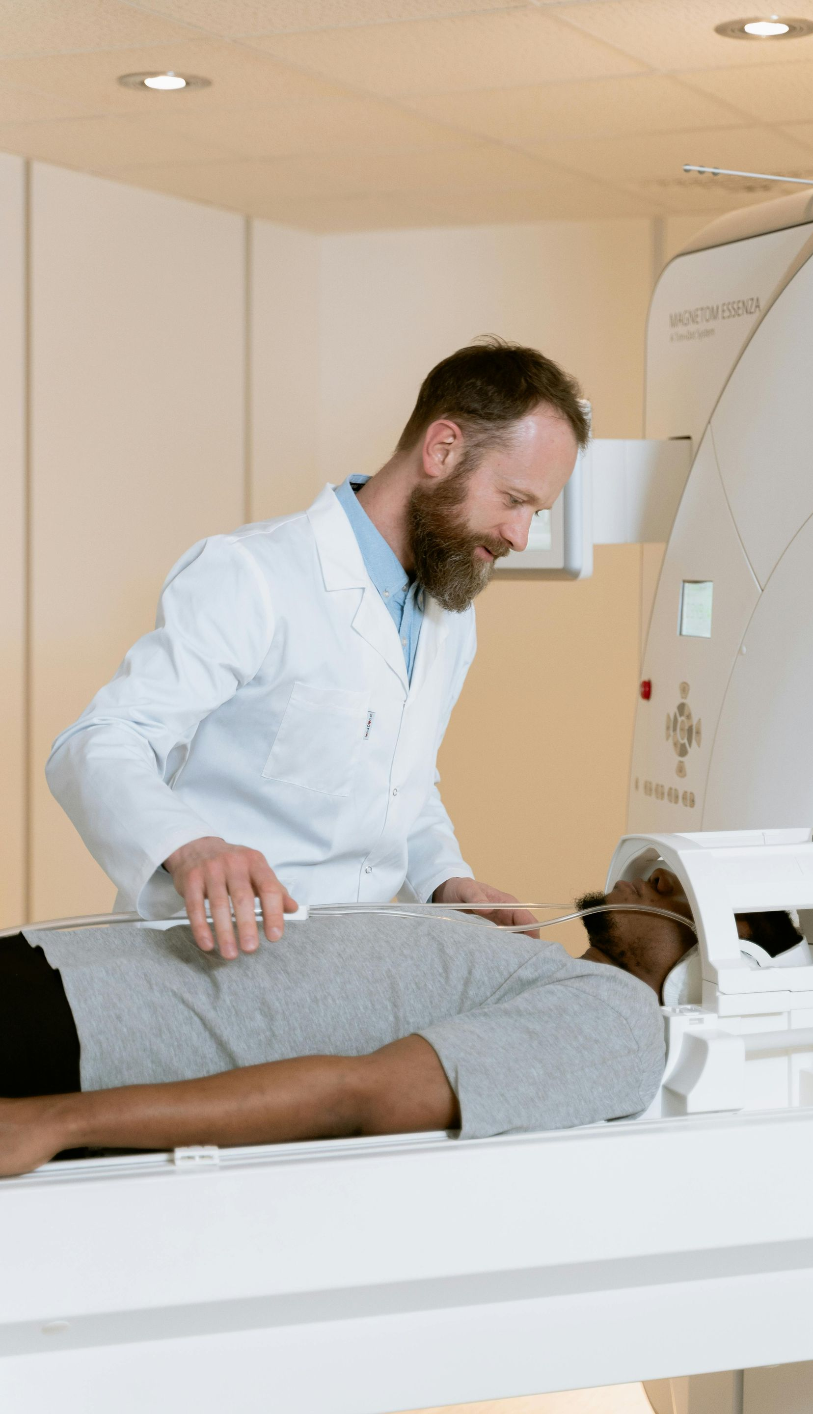 Doctor assisting a patient in an MRI machine. White lab coat, neutral expressions, medical setting.