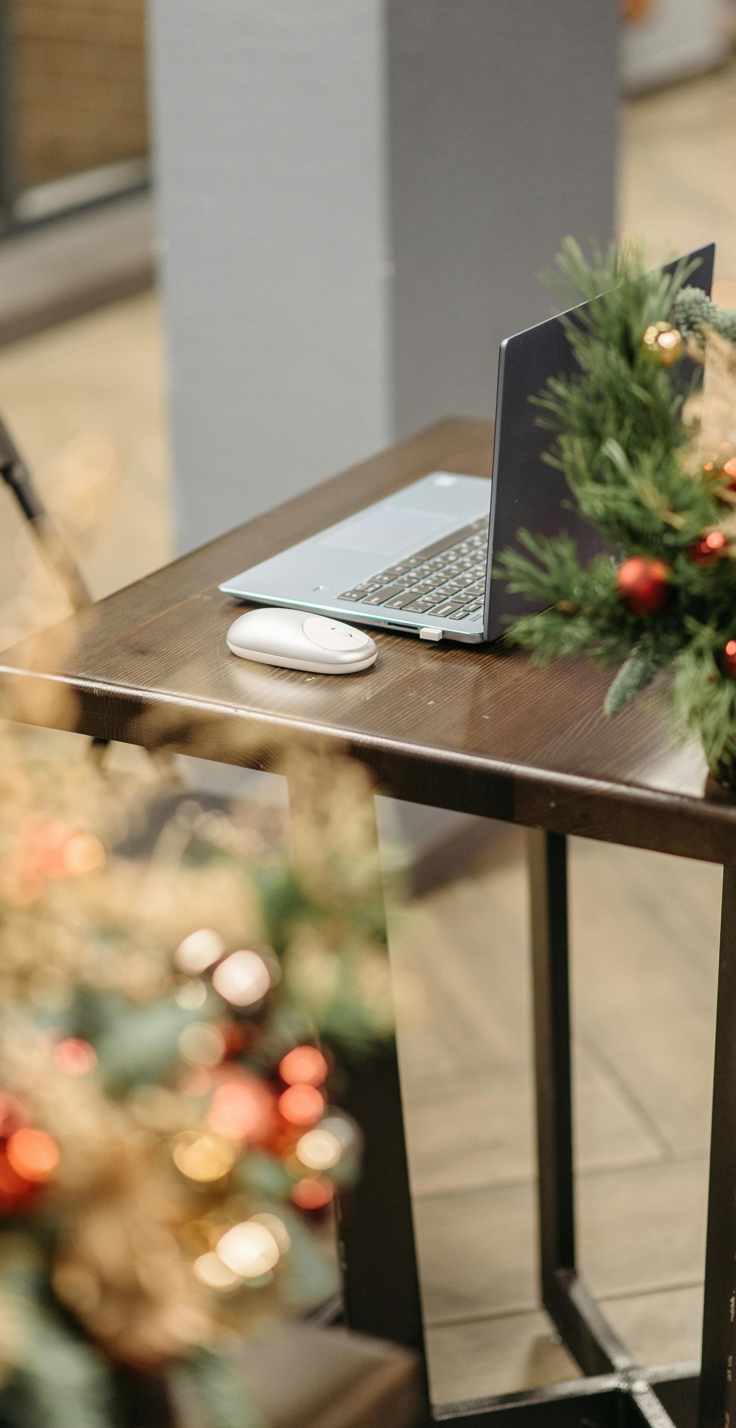 Laptop and mouse on a small table decorated with a Christmas wreath and ornaments.